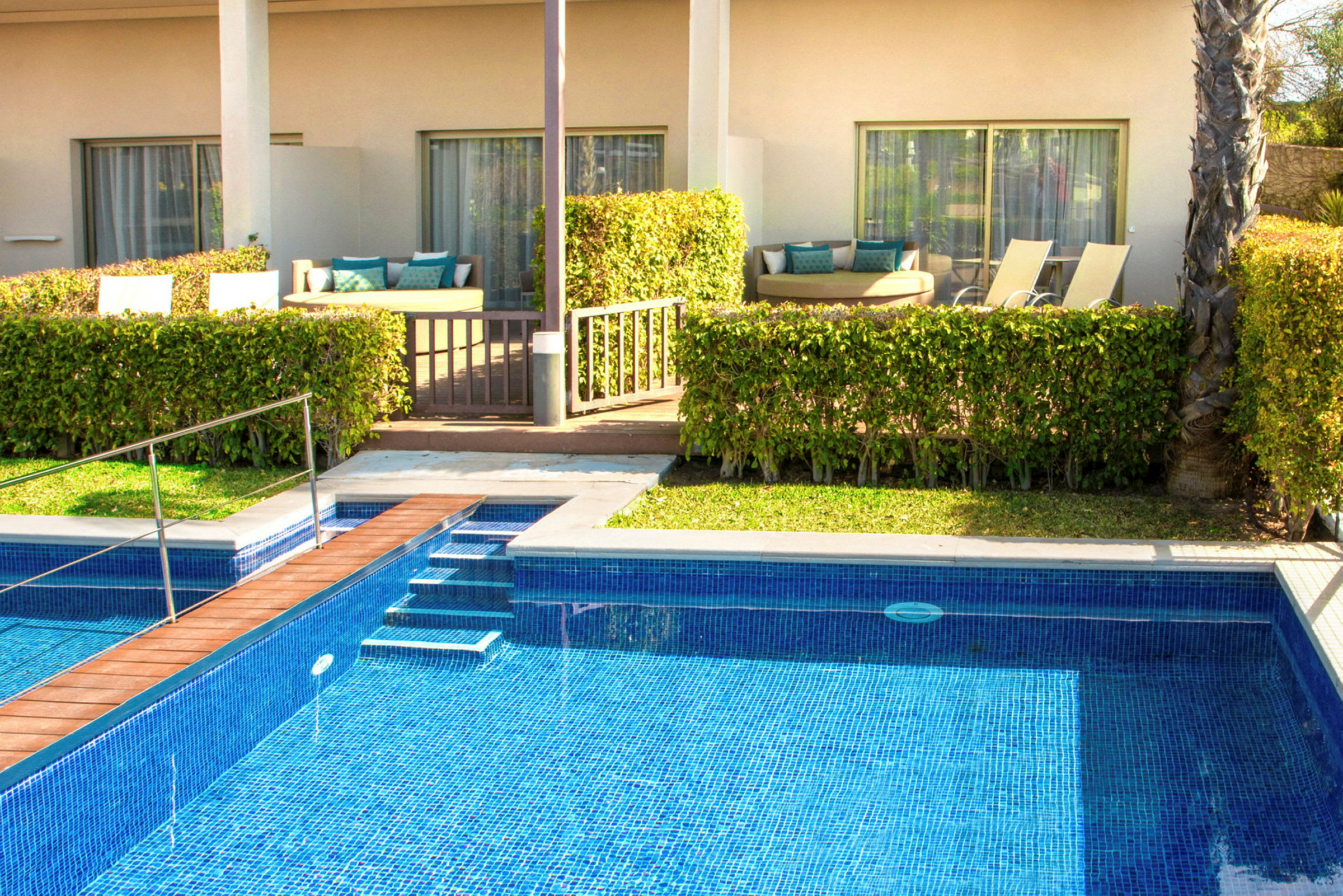 En swimmingpool foran en terrasse med siddepladser og liggestole. (AI-genereret tekst)