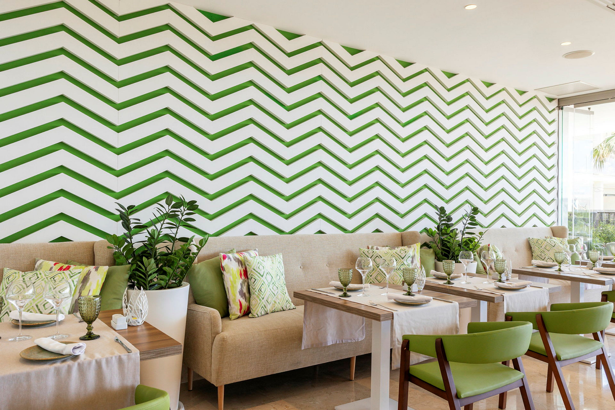 En restaurant med moderne interiør, grønne stole, lyse sofaer og en væg med grønne zigzag-mønstre. (AI-genereret tekst)