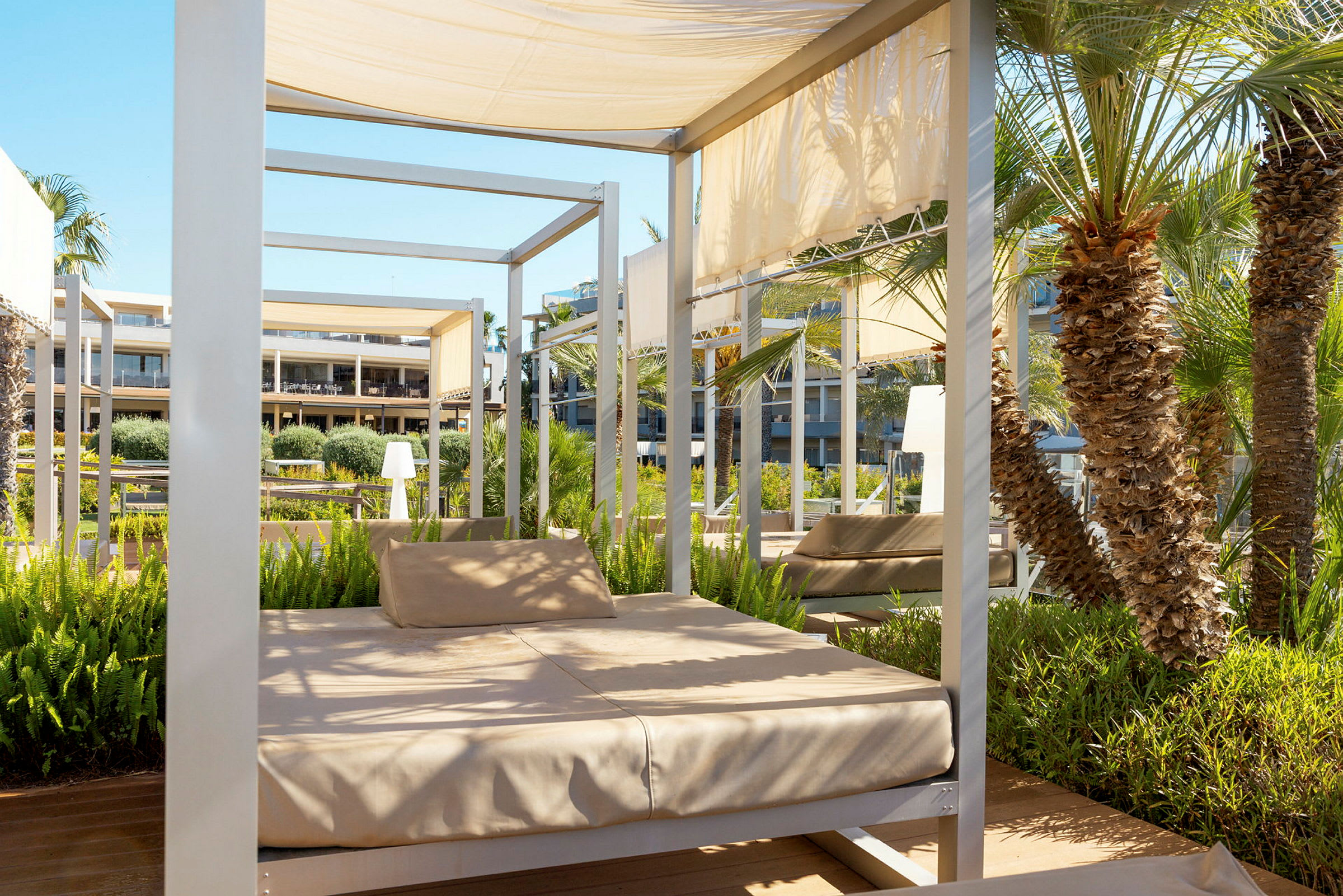 Afslapningsområder under baldakin i en resorts have med nærliggende palmetræer og vegetation. (AI-genereret tekst)