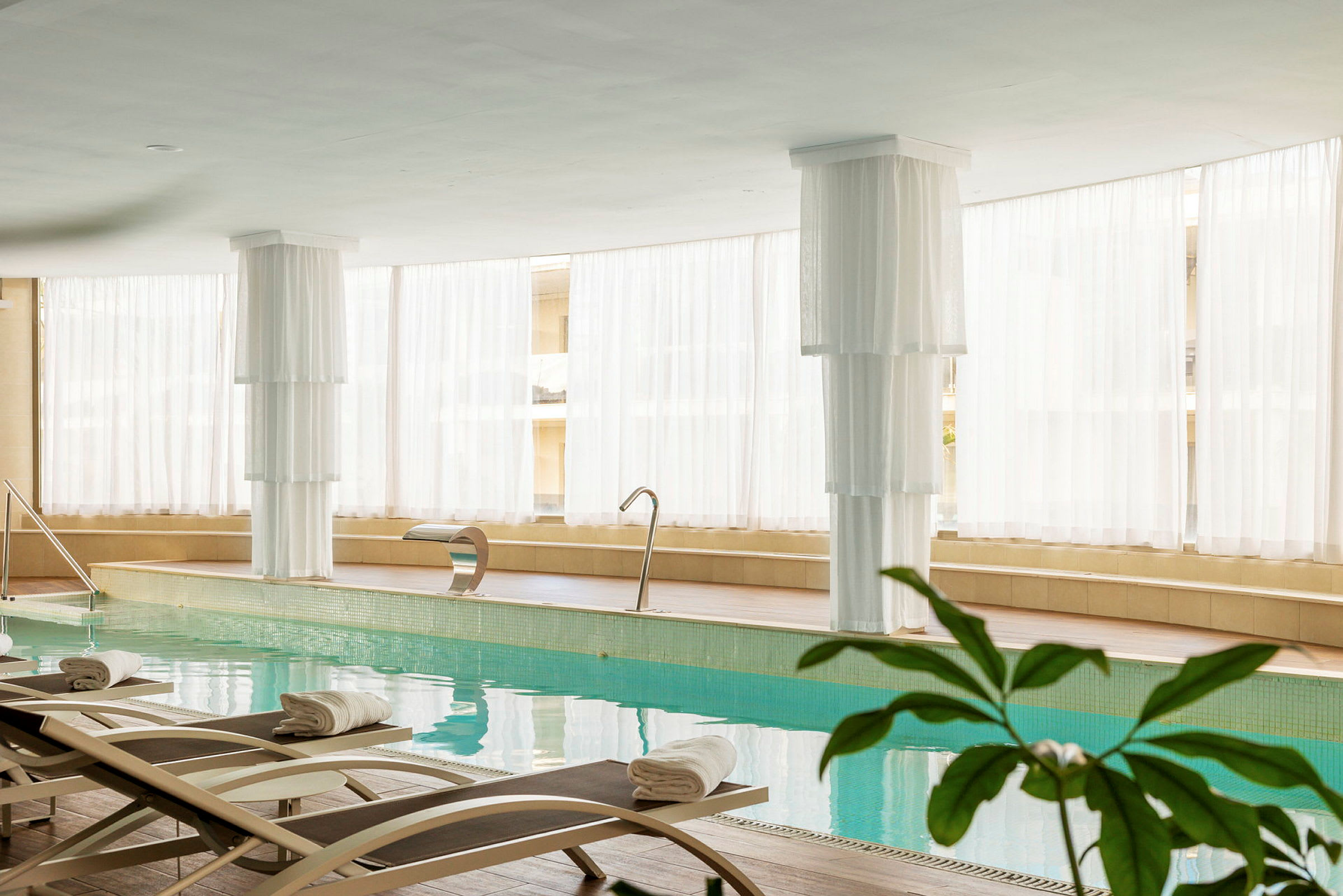 Interiør af et lyst spa med indendørs pool, liggestole og hvid indretning. (AI-genereret tekst)
