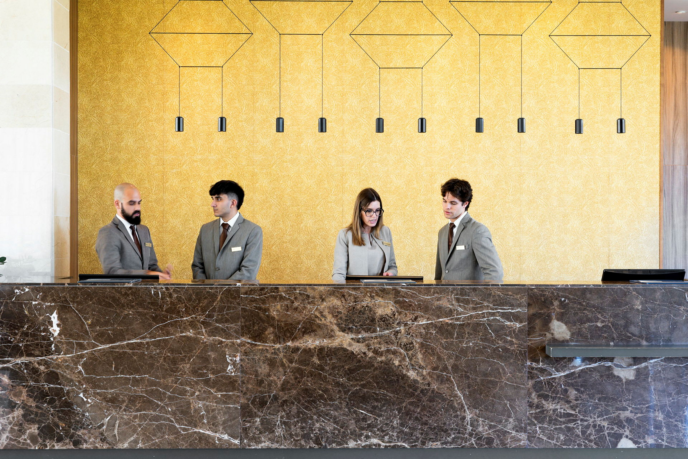 Personalet i hotelreceptionen iført uniformer ved en stor marmordisk. (AI-genereret tekst)