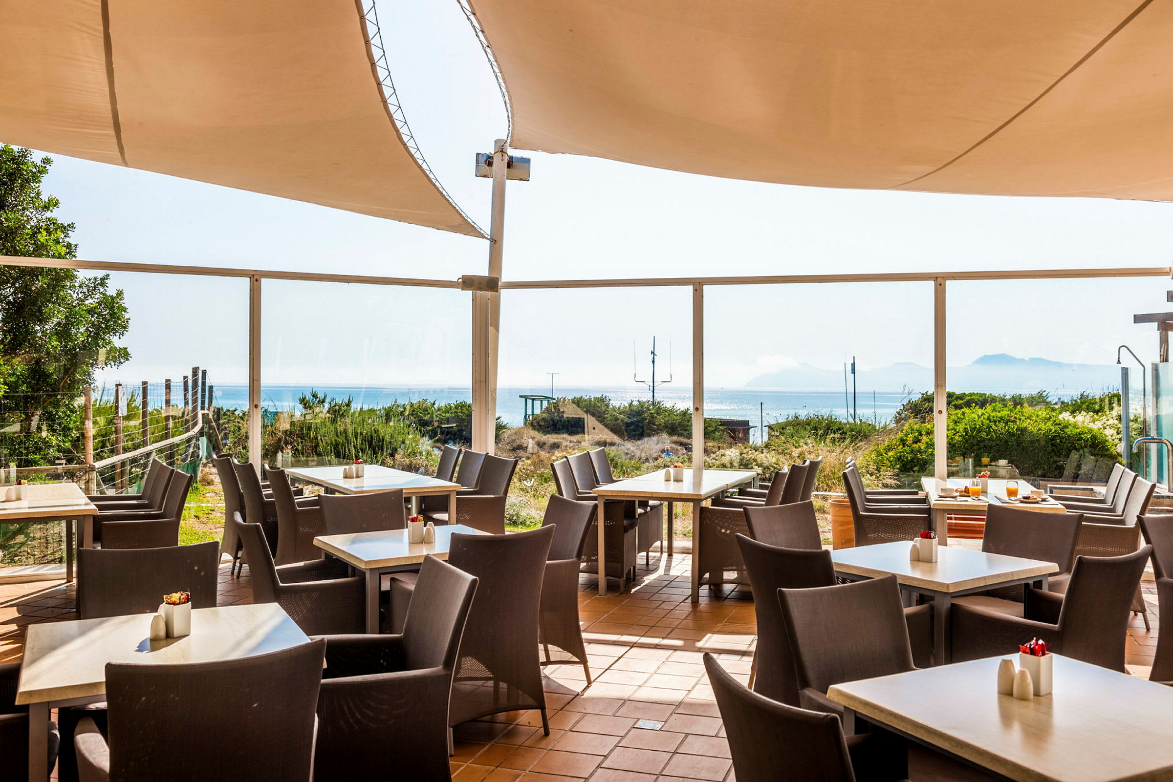 Billede af en udendørs terrasse med borde, stole og havudsigt. (AI-genereret tekst)