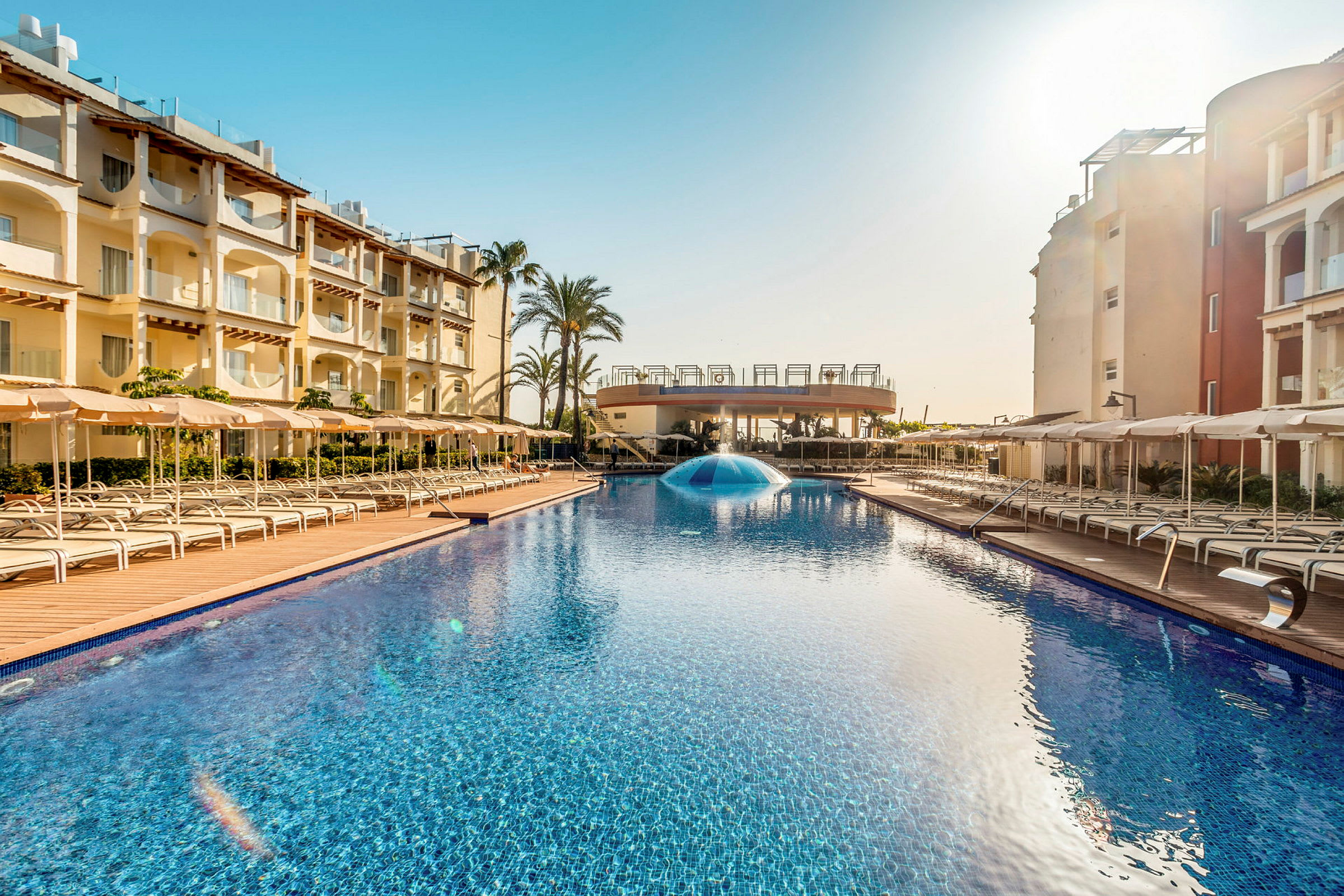 Udendørs pool ved hotel omgivet af liggestole og bygninger. (AI-genereret tekst)