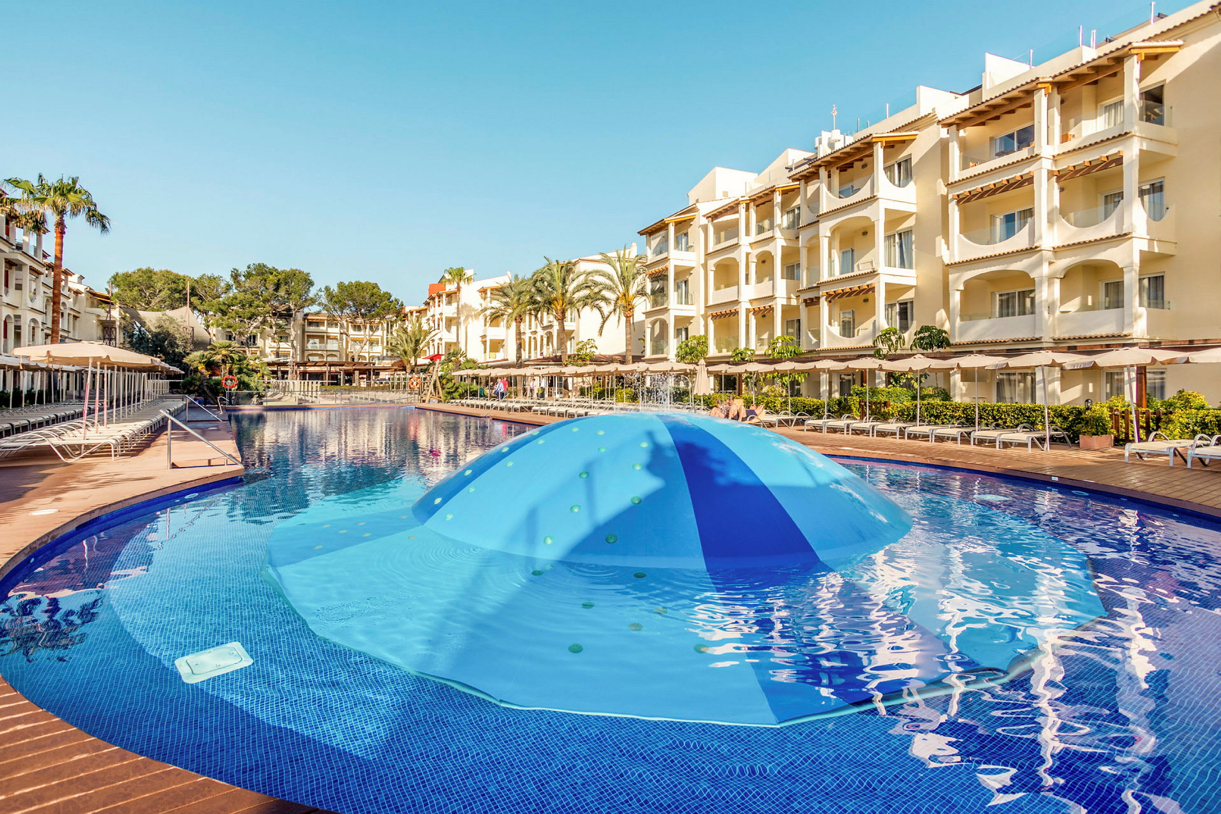Poolområde med blå vand og hotelbygning i baggrunden. (AI-genereret tekst)
