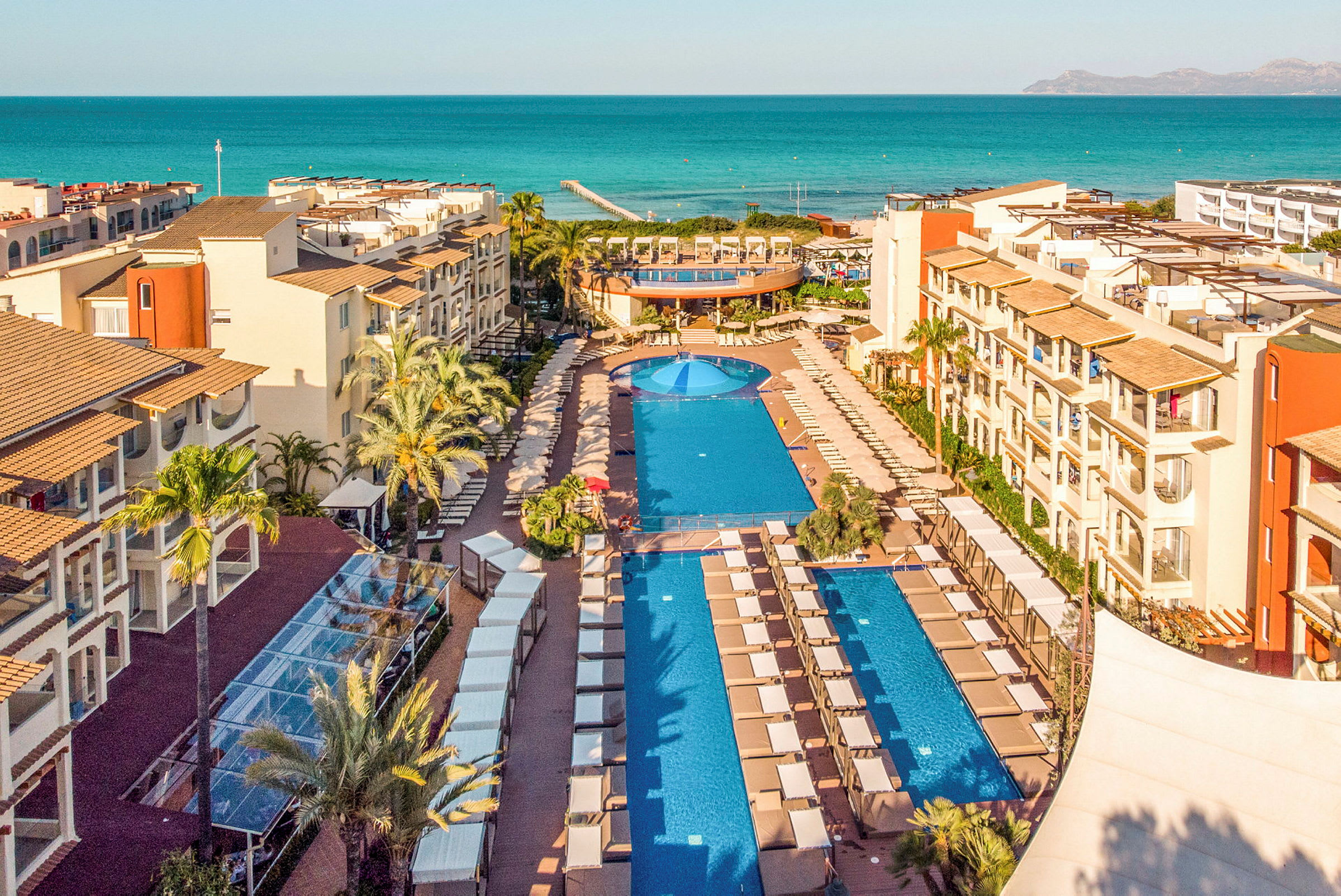Udsigt over en resort med swimmingpools og havet i baggrunden. (AI-genereret tekst)