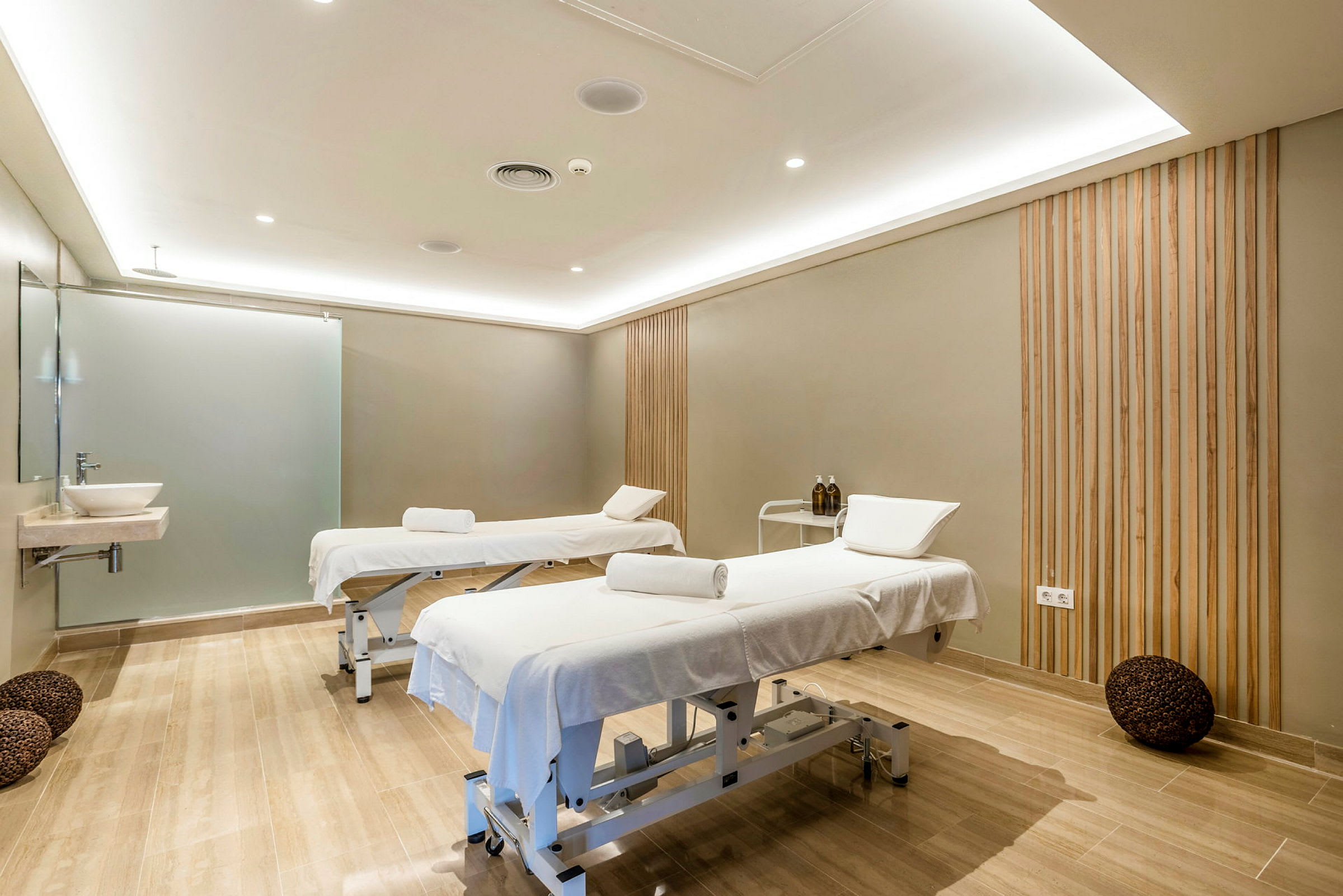 To massagebrikse med hvide håndklæder og puder i et behandlingsrum med trædetaljer på væggene. (AI-genereret tekst)