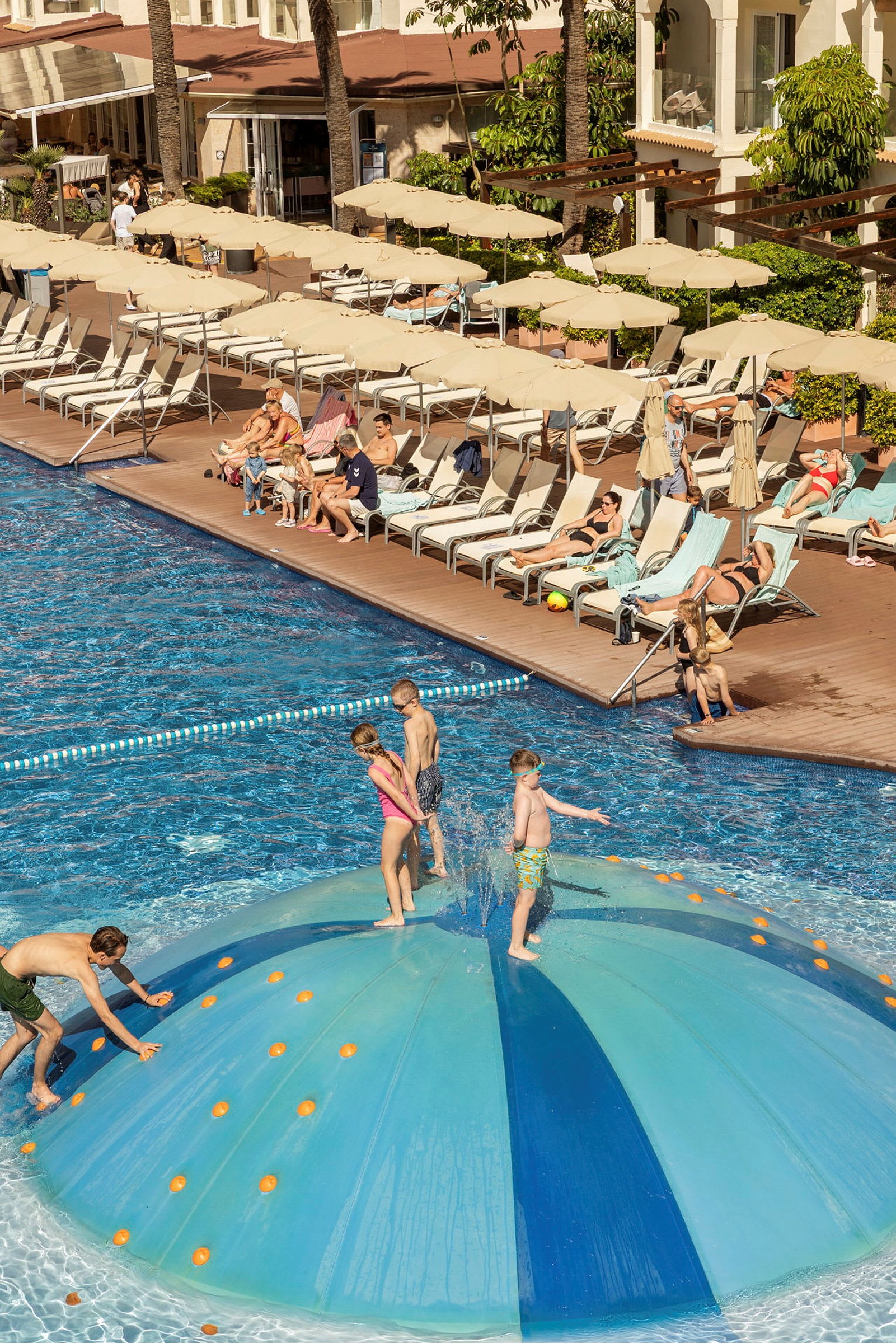 Folk nyder en udendørs pool med en vandlegestruktur i forgrunden. (AI-genereret tekst)