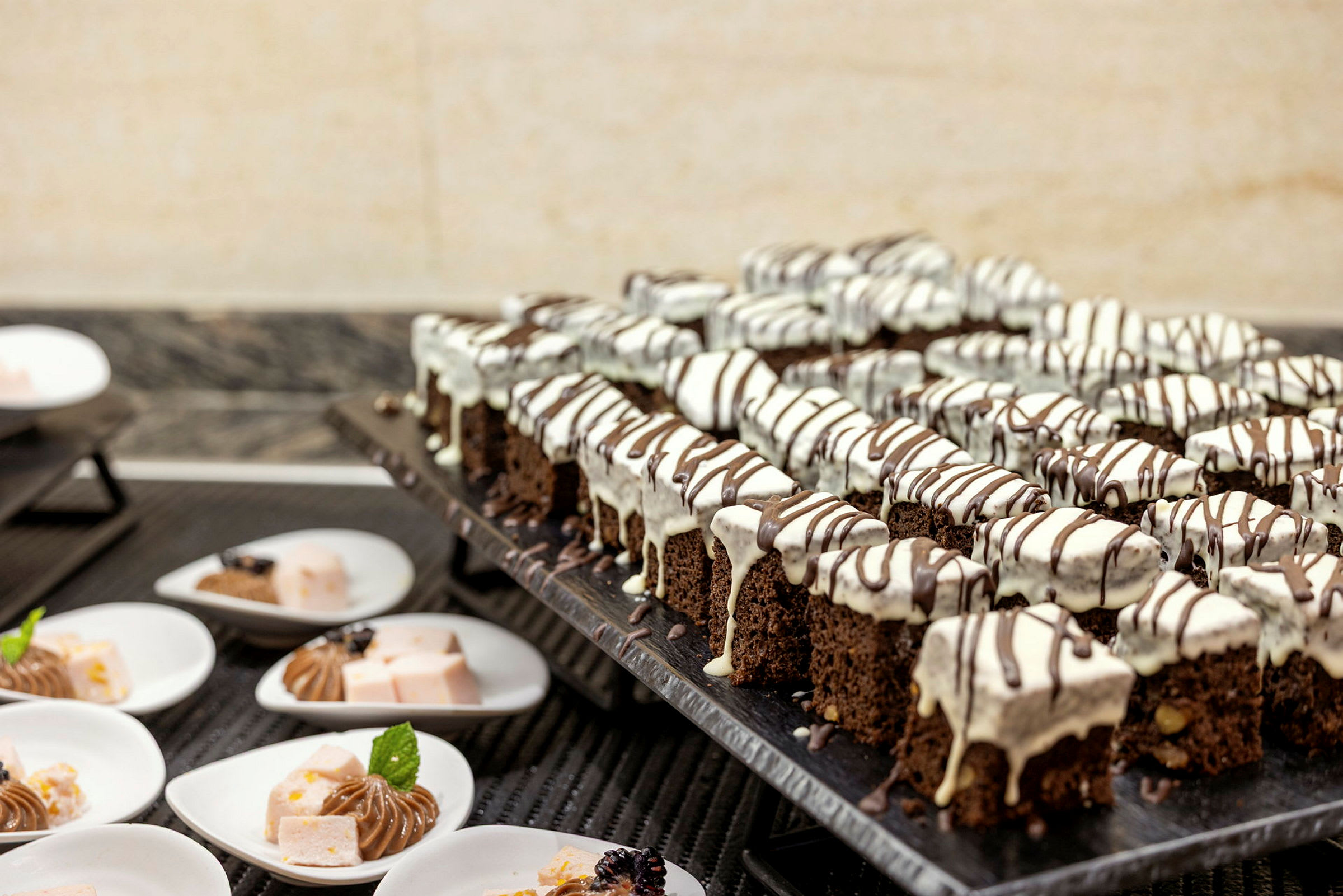 En buffet med chokoladekager dekoreret med hvid og mørk glasur på et serveringsbord. (AI-genereret tekst)