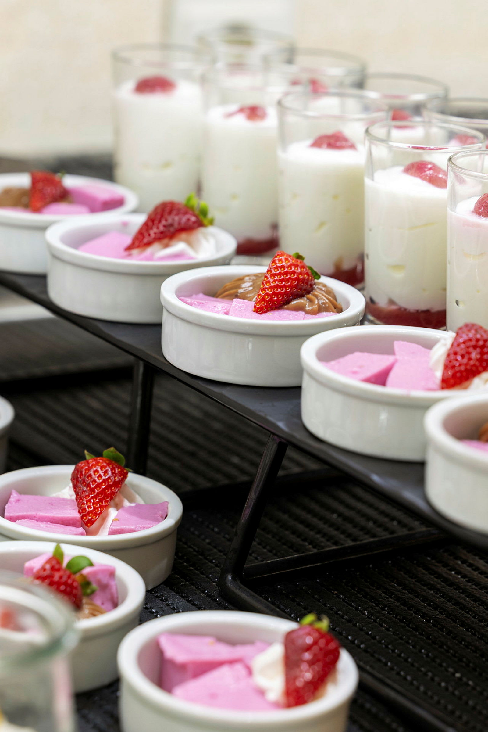 Et udvalg af desserter, herunder skåle med lyserød mousse og jordbær samt glas med hvid mousse og jordbær. (AI-genereret tekst)