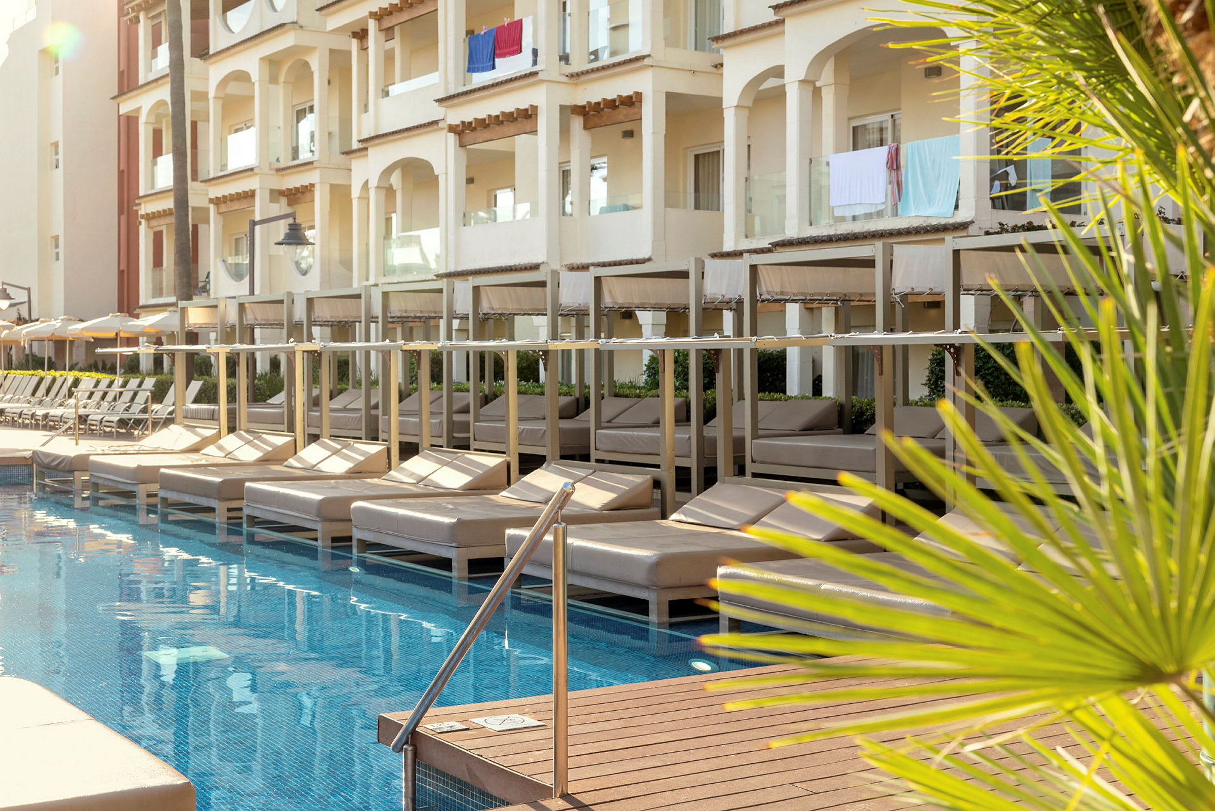 En pool med liggestole under skyggetage ved et hotel med altaner. (AI-genereret tekst)