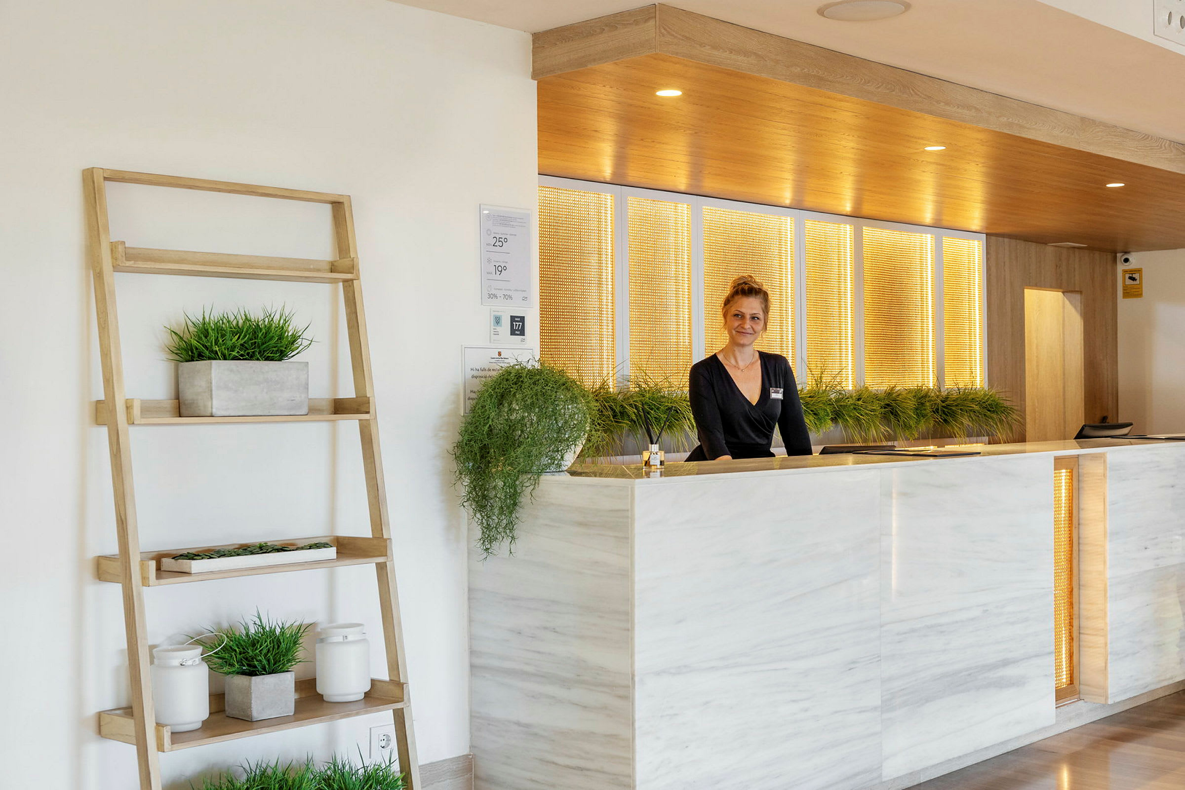 Reception med marmorpanel og planter. En person står bag skranken. (AI-genereret tekst)