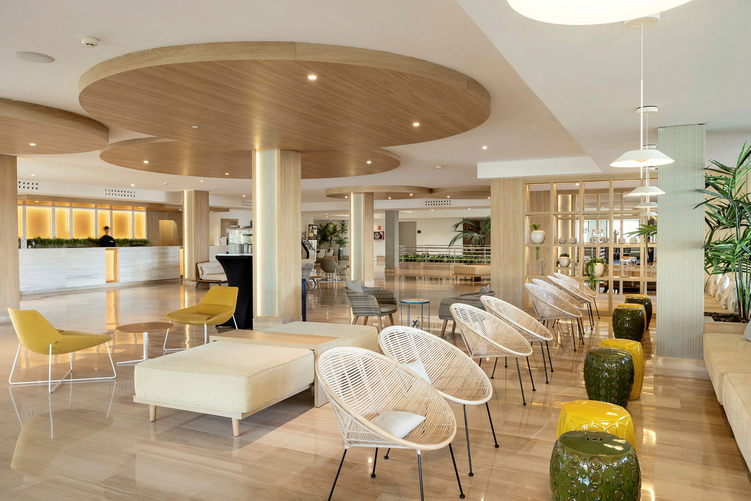 En lys og moderne lounge med træelementer, stole, borde og rigelig grøn beplantning. (AI-genereret tekst)