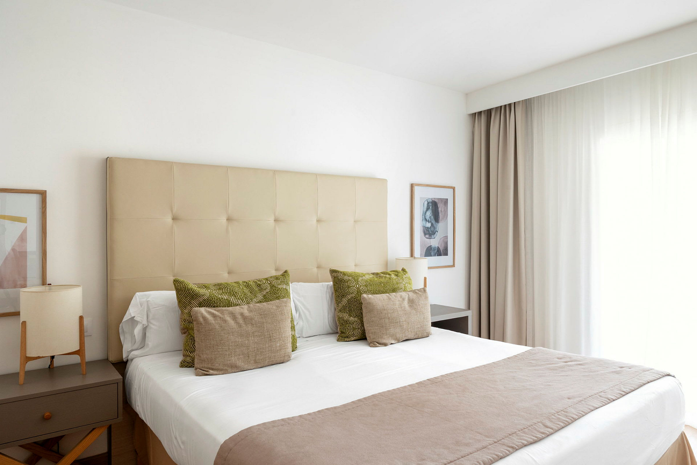 Et lyst og elegant hotelværelse med en redt seng. Gardiner til højre og natbord til venstre. (AI-genereret tekst)
