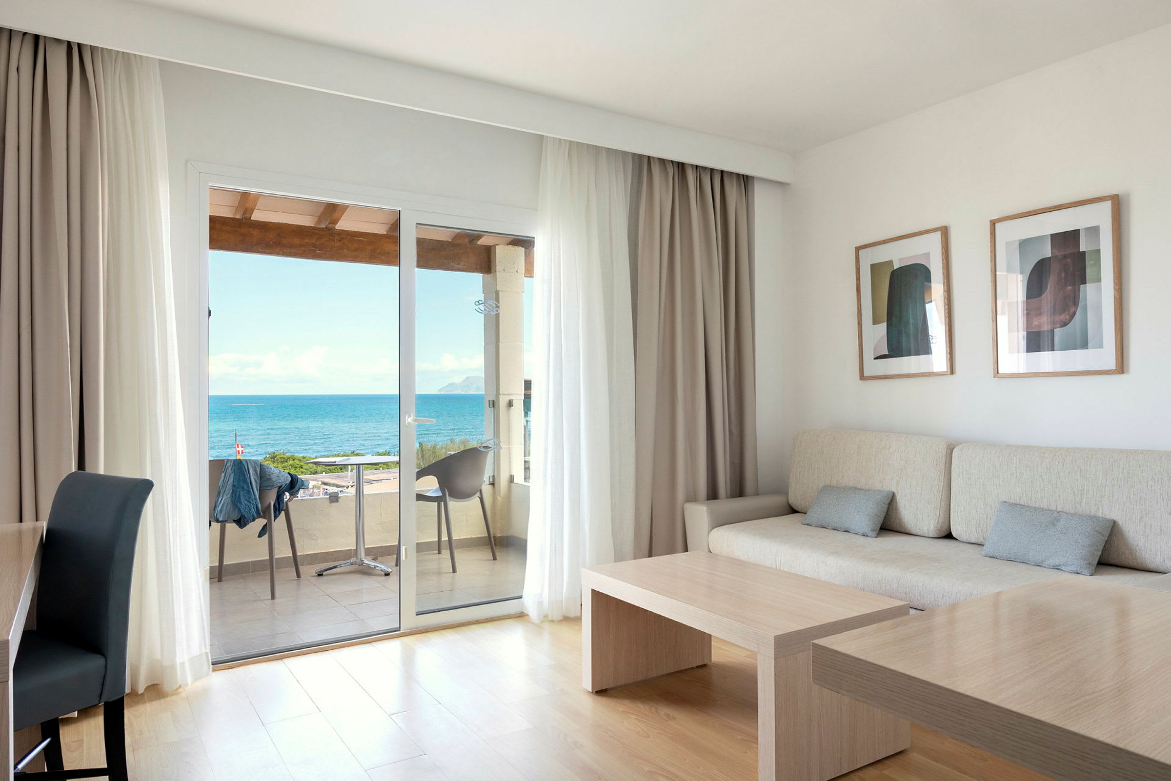 Et lyst rum med sofa, bord og store glasdøre, der fører ud til en balkon med udsigt over havet. (AI-genereret tekst)