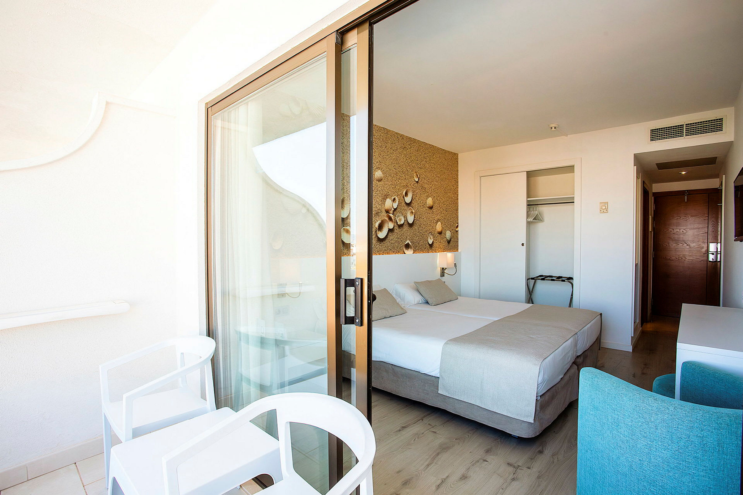 Hotelværelse med balkon, dobbeltseng og indretning i lyse nuancer. (AI-genereret tekst)