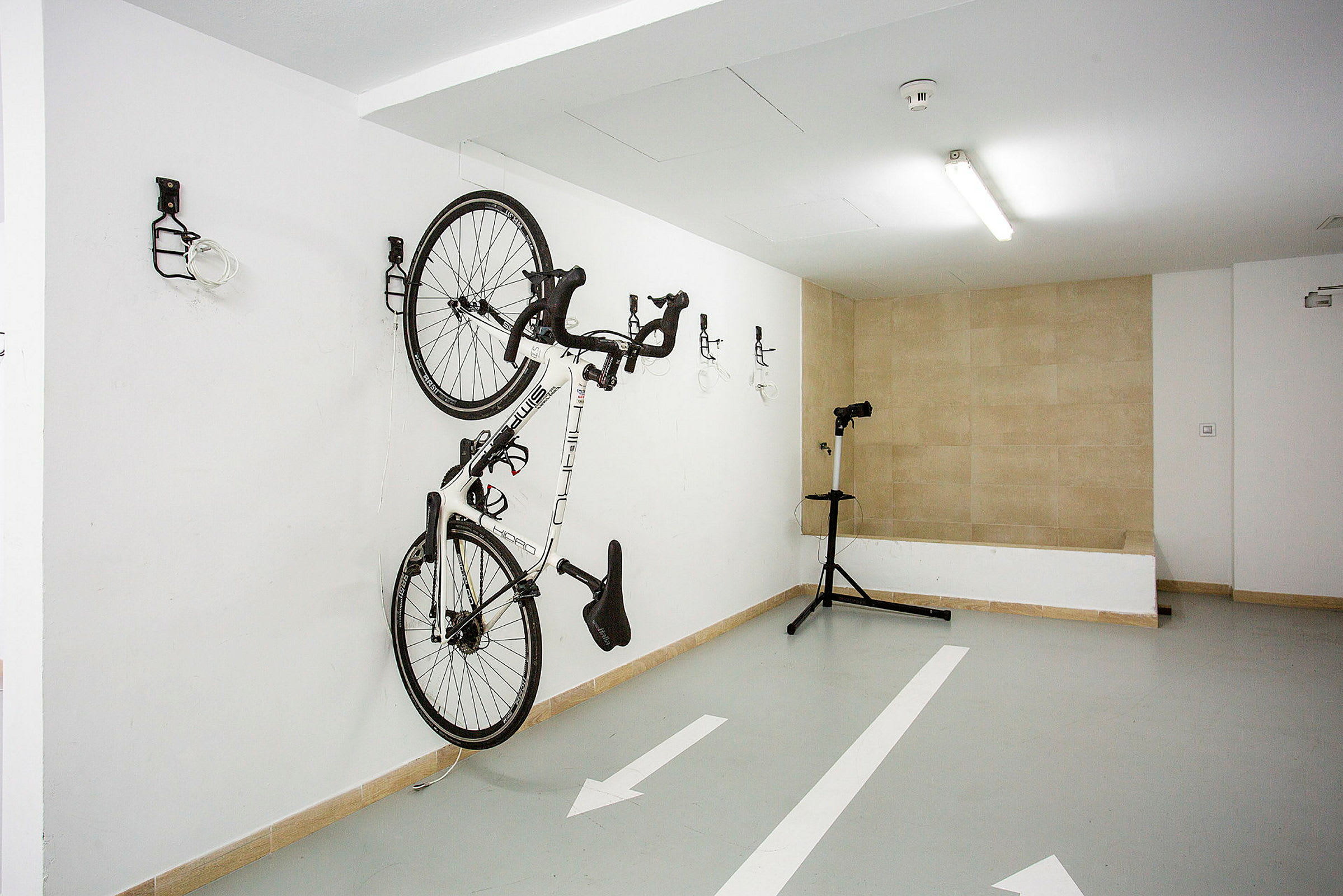 En cykel hænger på væggen i en garage. Et reparationsstativ står ved siden af. (AI-genereret tekst)