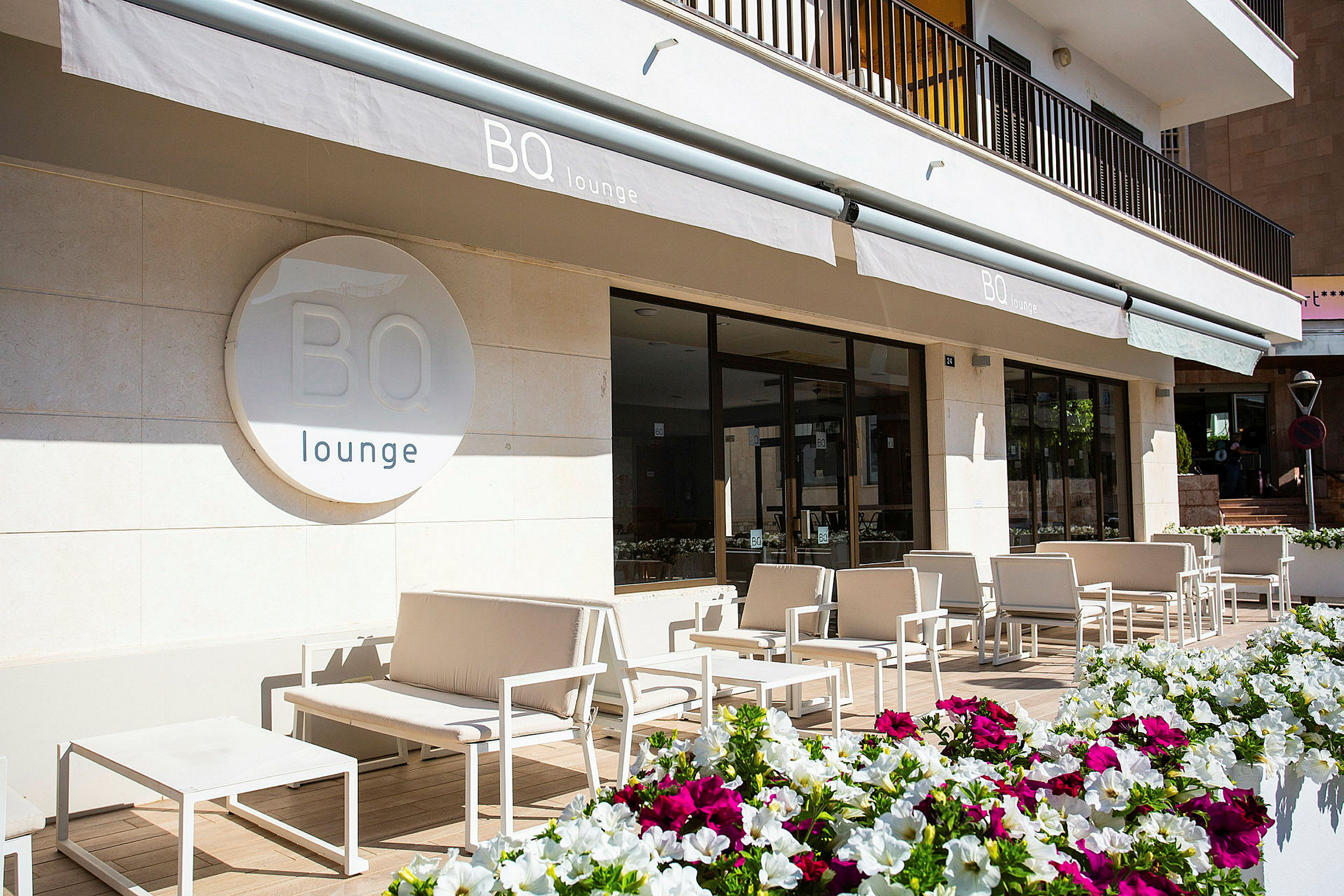 Billede af en udendørs lounge med hvide moderne møbler og farverige blomster i forgrunden. (AI-genereret tekst)