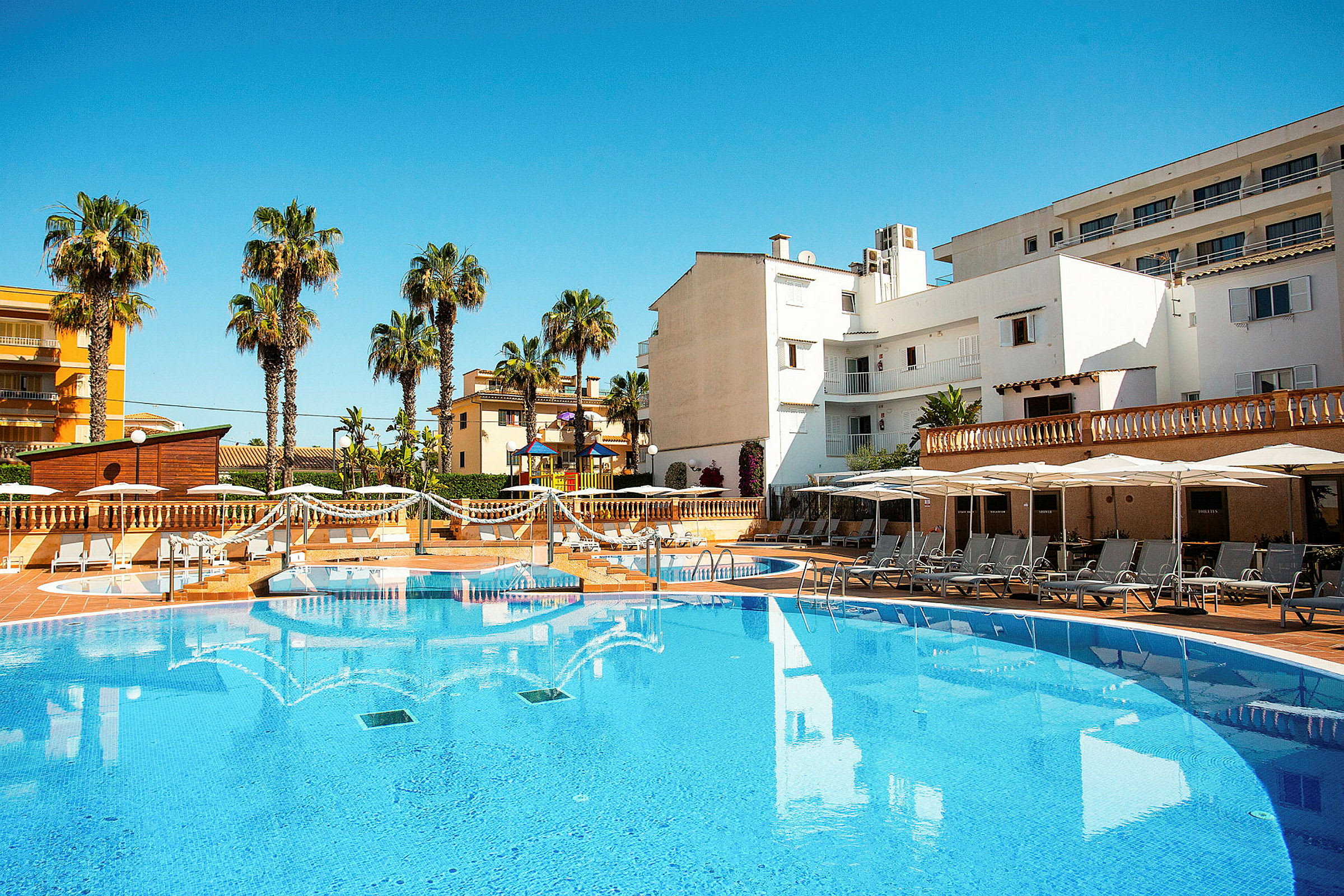 Udendørs swimmingpool med liggestole og parasoller ved et hotelområde. (AI-genereret tekst)