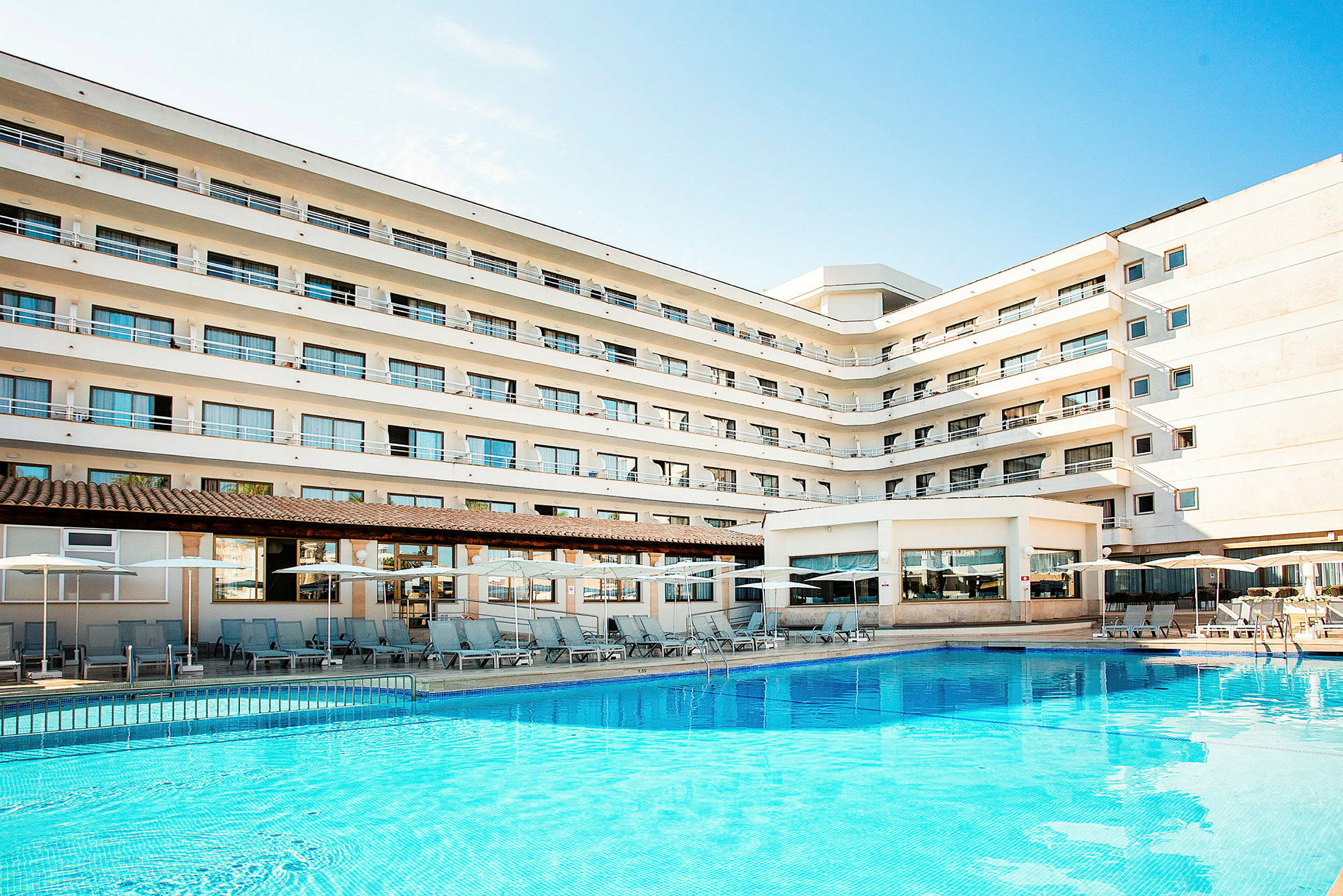 Et billede af et hotel med flere etager og en pool foran bygningen. (AI-genereret tekst)