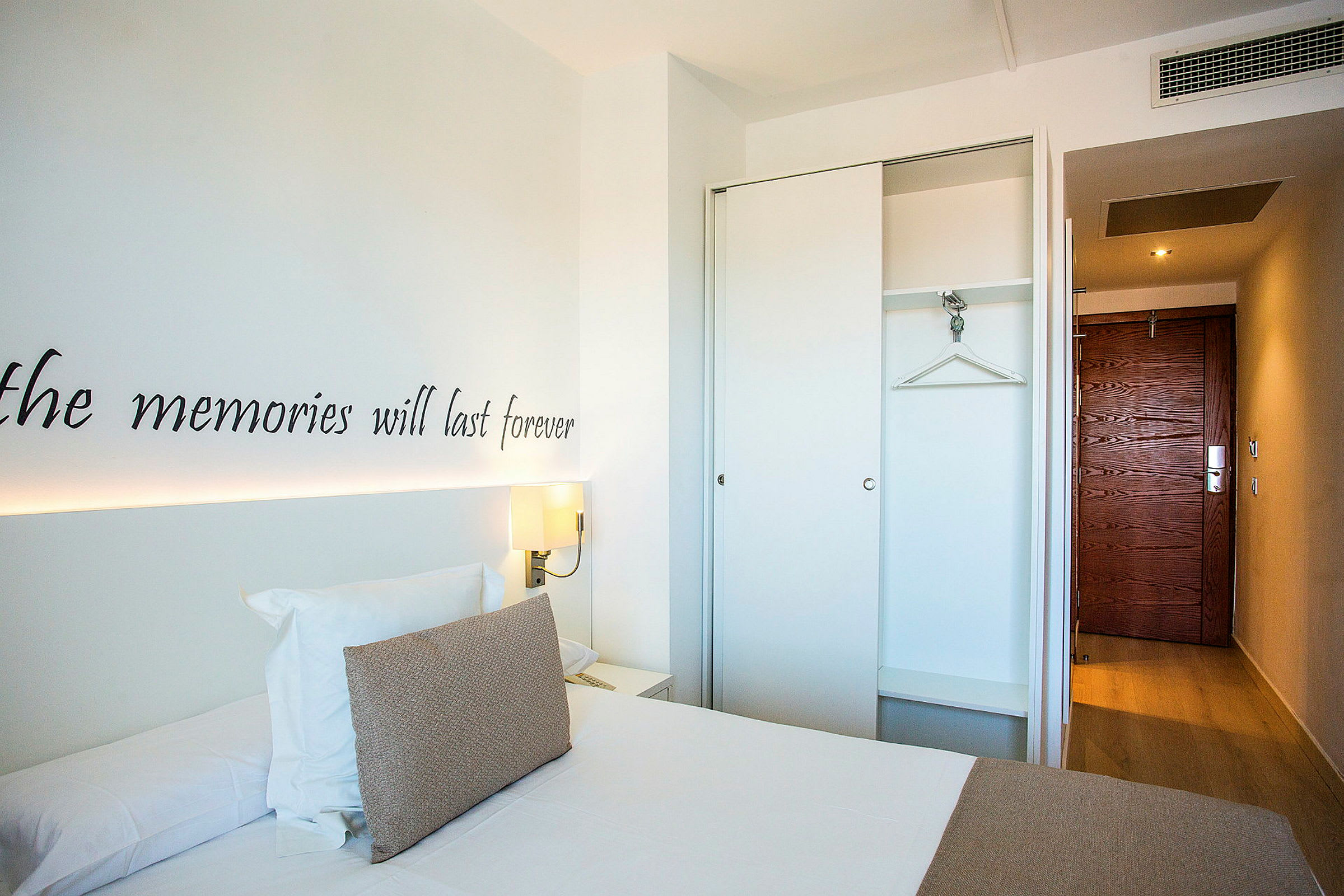 Et hotelværelse med en seng, garderobe og indgangsdør. (AI-genereret tekst)