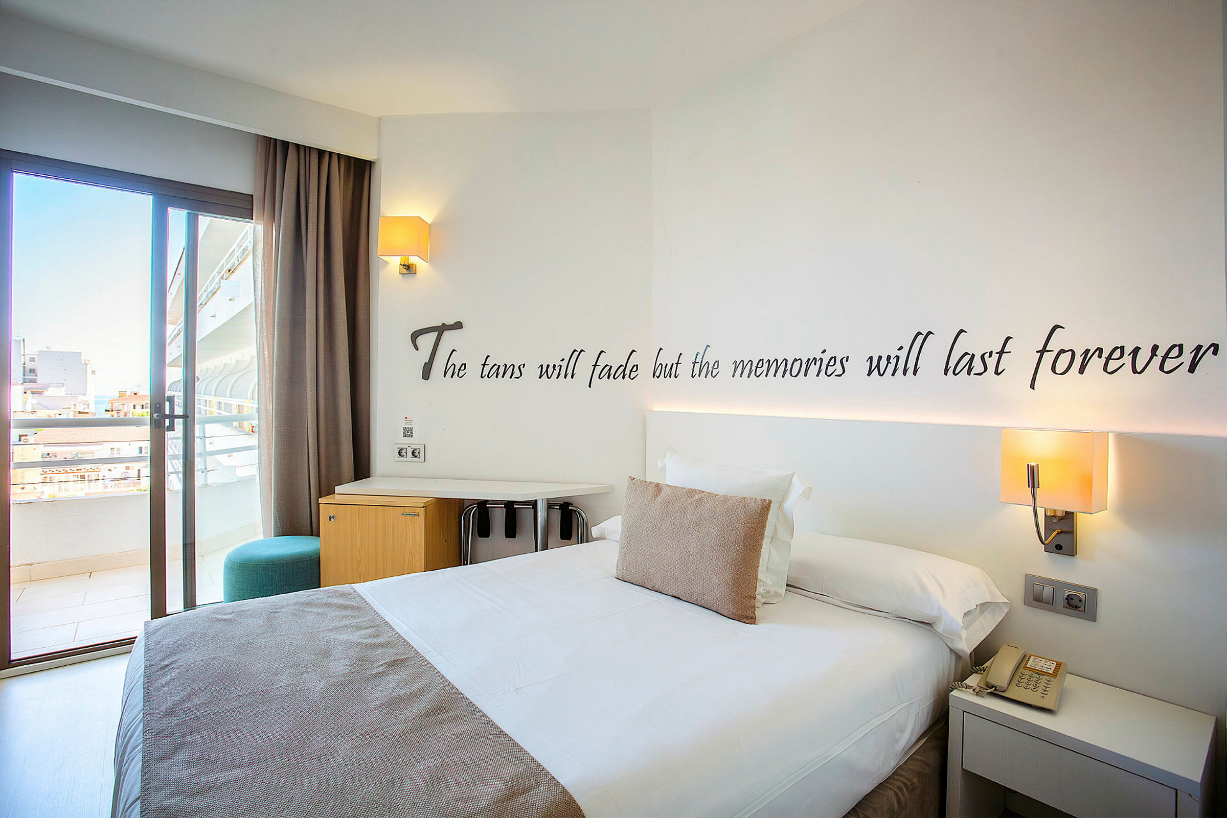 Hotelværelse med en dobbeltseng, skrivebord og altandør. (AI-genereret tekst)