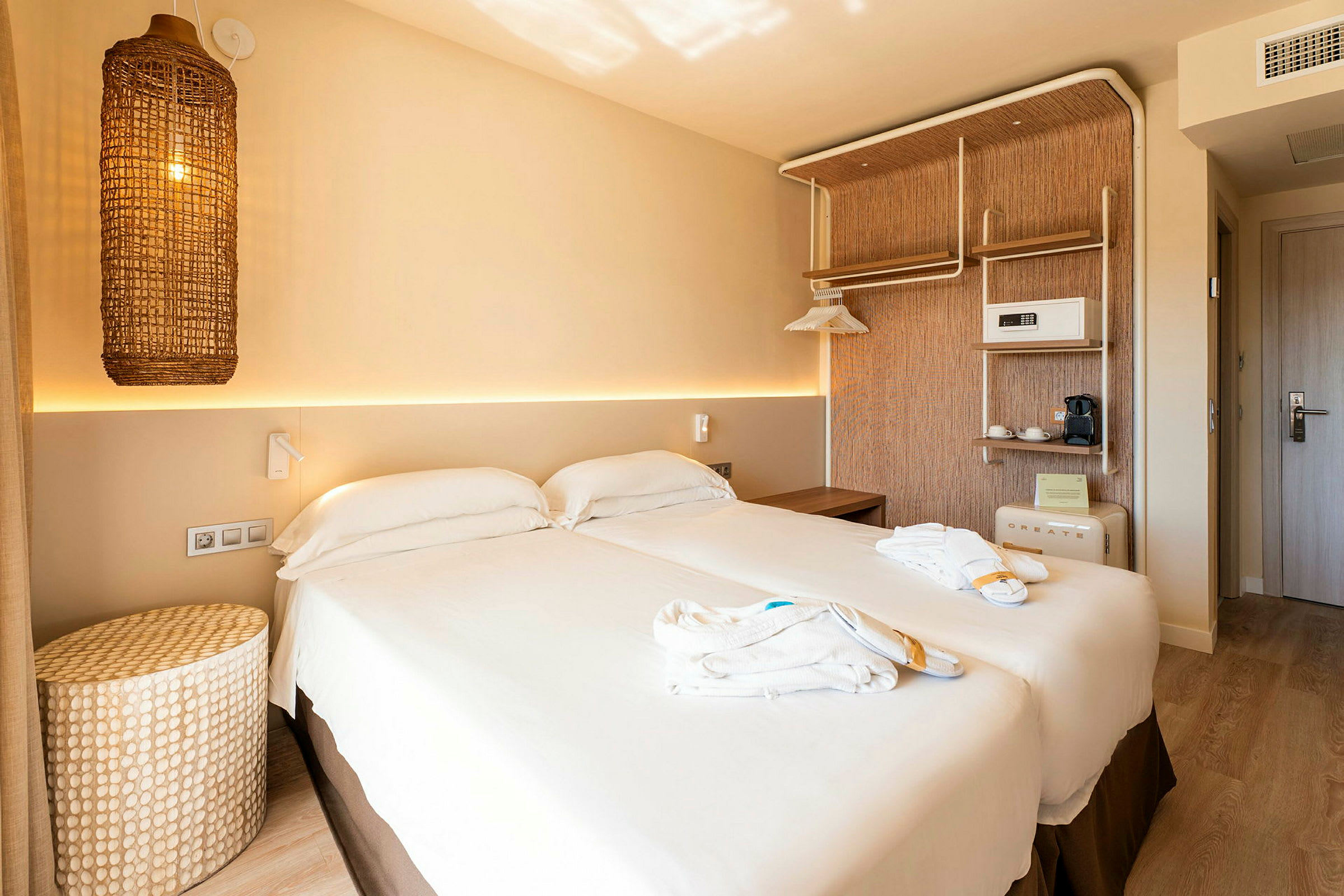 Et hotelværelse med en dobbeltseng, lys indretning og en flettet lampe hængende på væggen. (AI-genereret tekst)