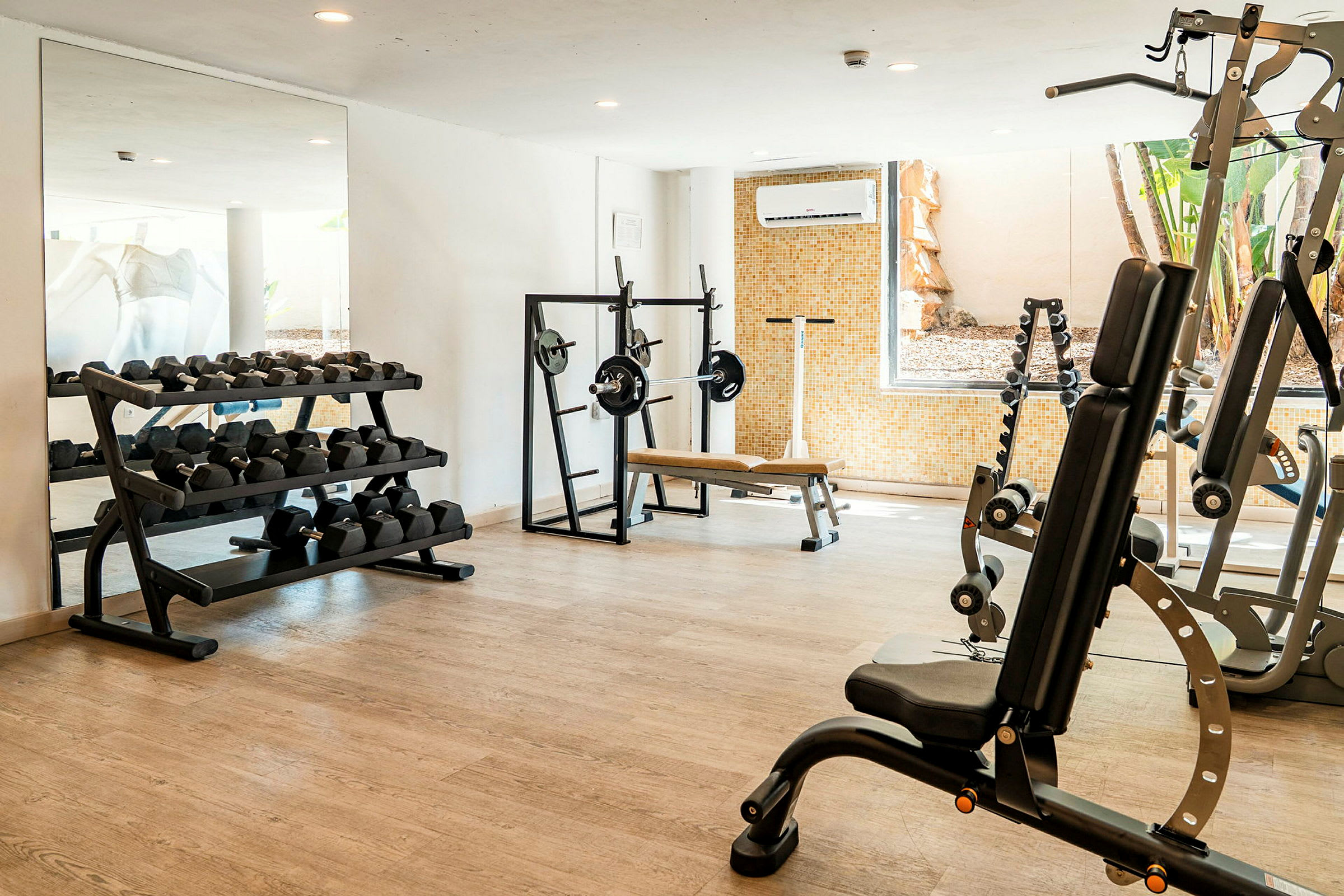 Et fitnesscenter med træningsudstyr som håndvægte, træningsbænk og styrketræningsmaskiner. (AI-genereret tekst)