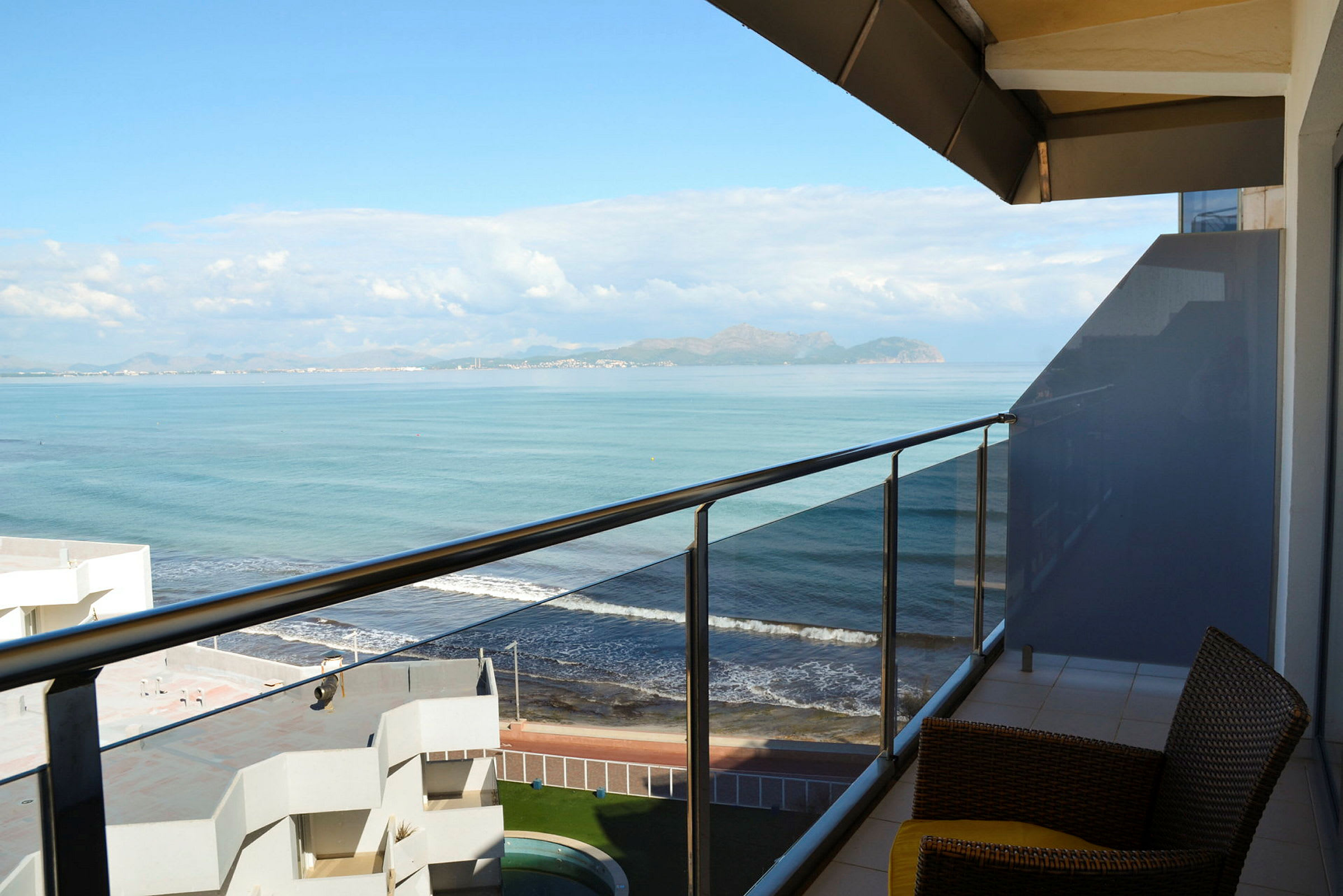 Udsigt fra en balkon ud mod havet med en strand nedenfor. (AI-genereret tekst)
