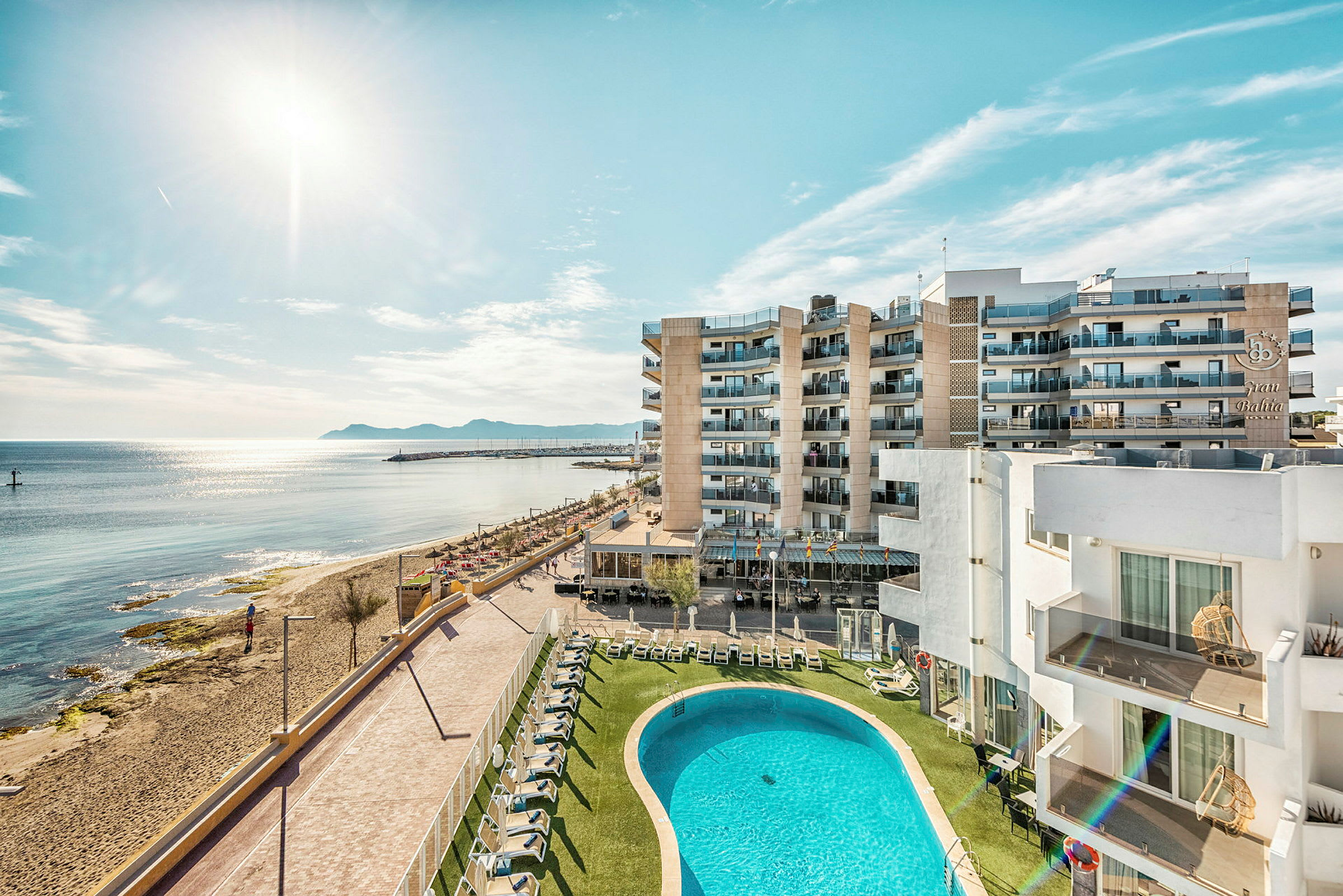 Hotelbygninger ved stranden med poolområde og hav i baggrunden. (AI-genereret tekst)