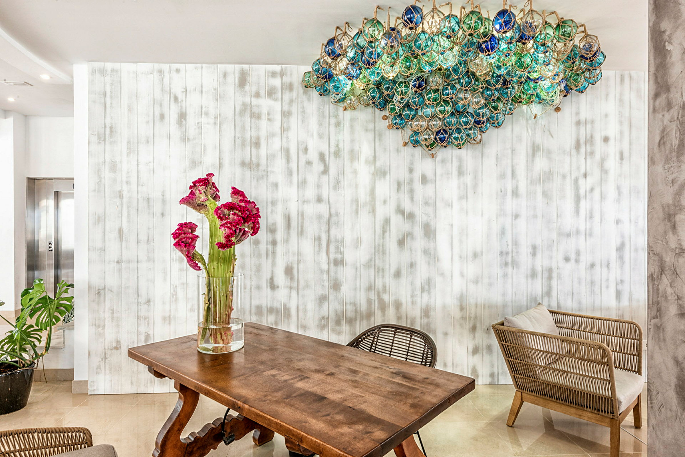 Et træbord med en vase med lyserøde blomster, samt stole ved siden af i et rum med lys indretning og en unik loftlampe. (AI-genereret tekst)