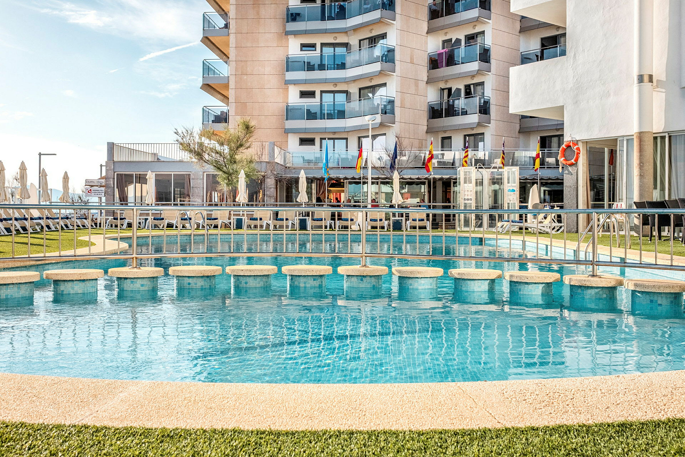 Udendørs pool foran et hotel med altaner. (AI-genereret tekst)