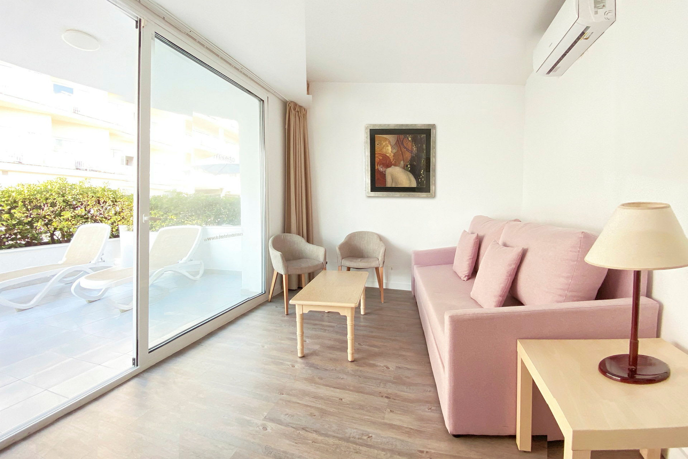 Sofa med pink betræk, sofabord, to stole og vindue med udsigt til terrassen. (AI-genereret tekst)