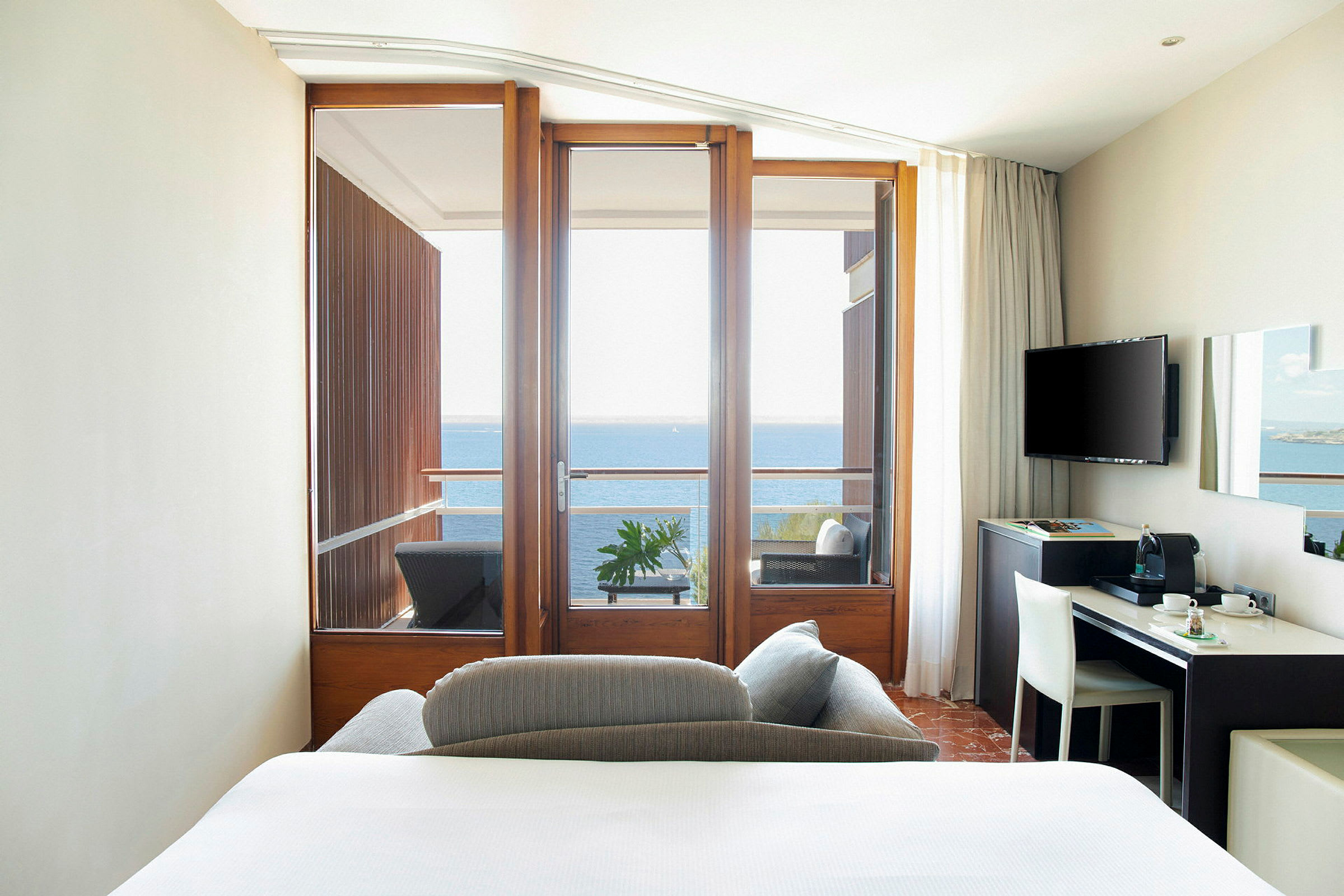 Hotelværelse med balkon ud mod havet og en enkel skrivebordsstation. (AI-genereret tekst)