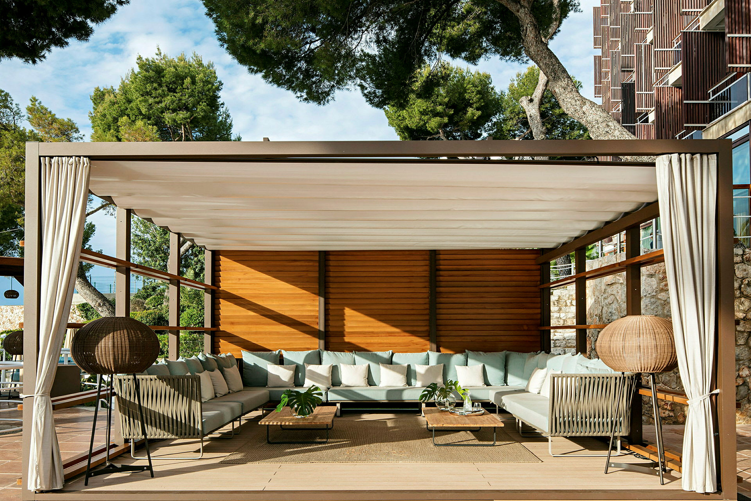 En lounge med sofaer, borde og gardiner under en pergola. (AI-genereret tekst)