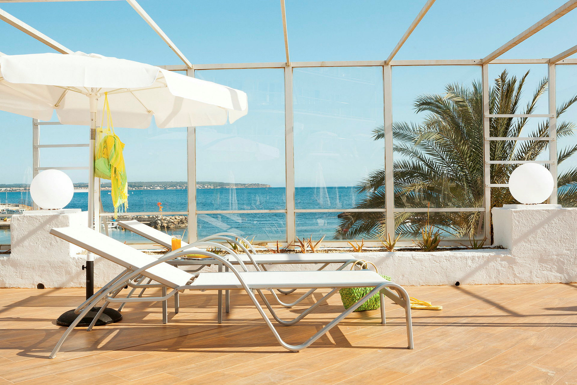 To liggestole og en hvid parasol på en terrasse med udsigt over havet. (AI-genereret tekst)