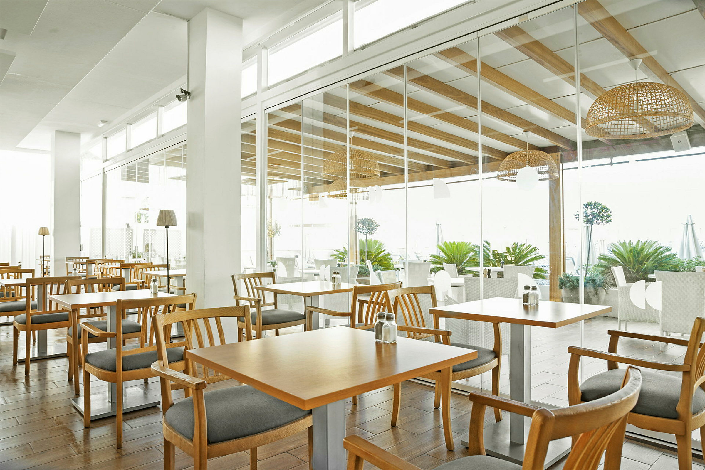 En restaurant med træborde og stole, lys indretning og store glaspartier. (AI-genereret tekst)