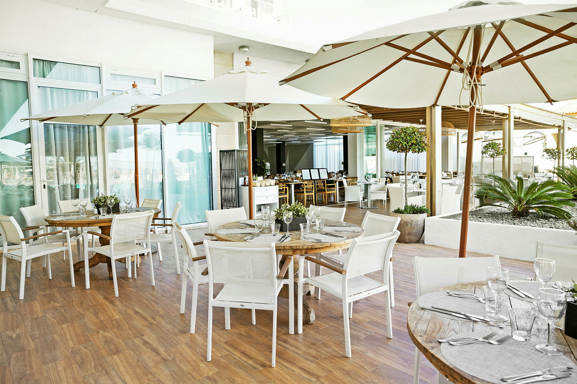 Borde med parasoller og stole på en restaurantterrasse. Glas og bestik er placeret på bordene. (AI-genereret tekst)