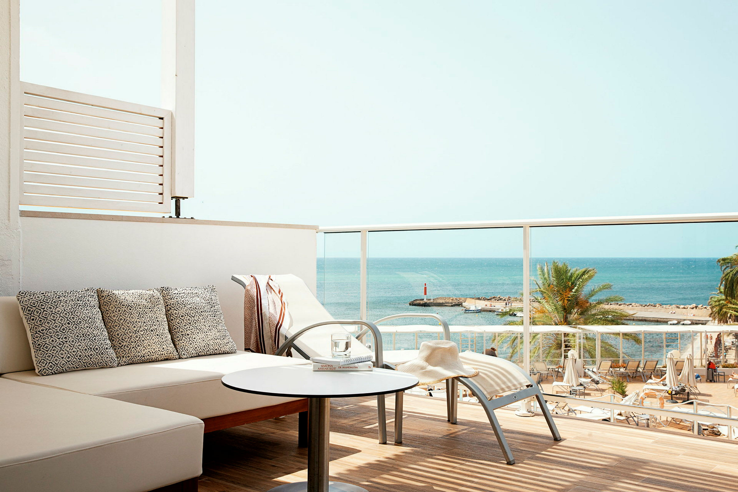 Udsigt fra en balkon med siddepladser mod havet og stranden. (AI-genereret tekst)