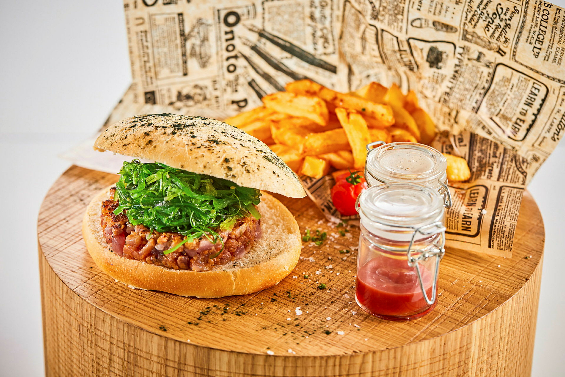 En hamburger med salat på et træbord sammen med pommes frites og glaskrukker med sovs. (AI-genereret tekst)