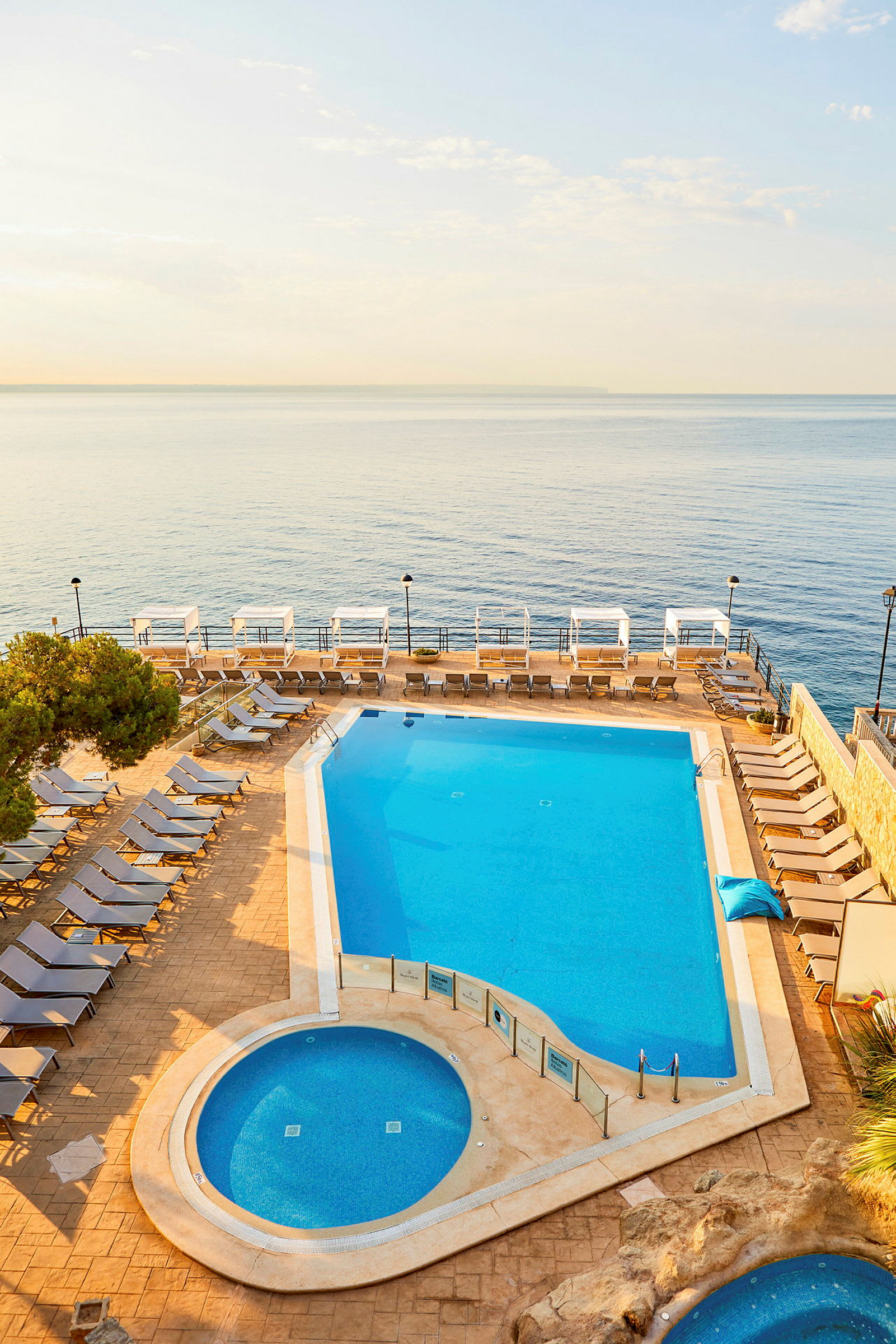 Billede af en udendørs swimmingpool ved havet, omgivet af liggestole og cabanas. (AI-genereret tekst)