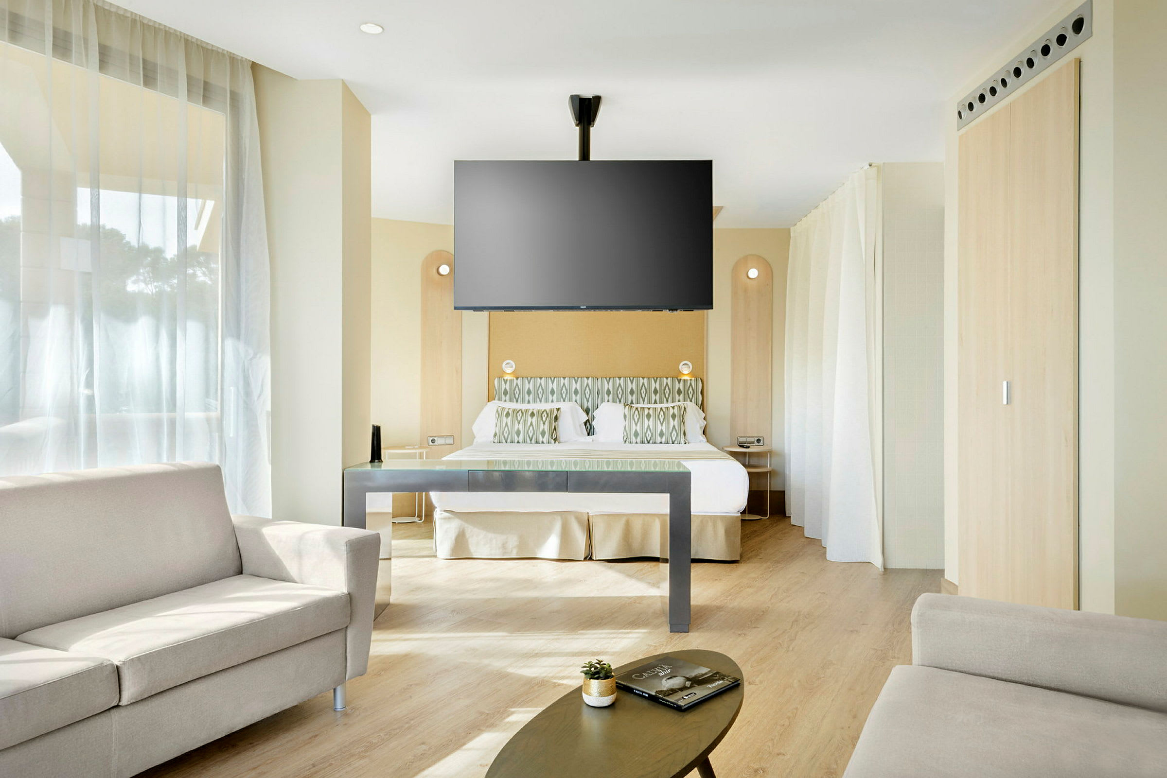 Et hotelværelse med seng, sofa og vægmonteret TV. (AI-genereret tekst)