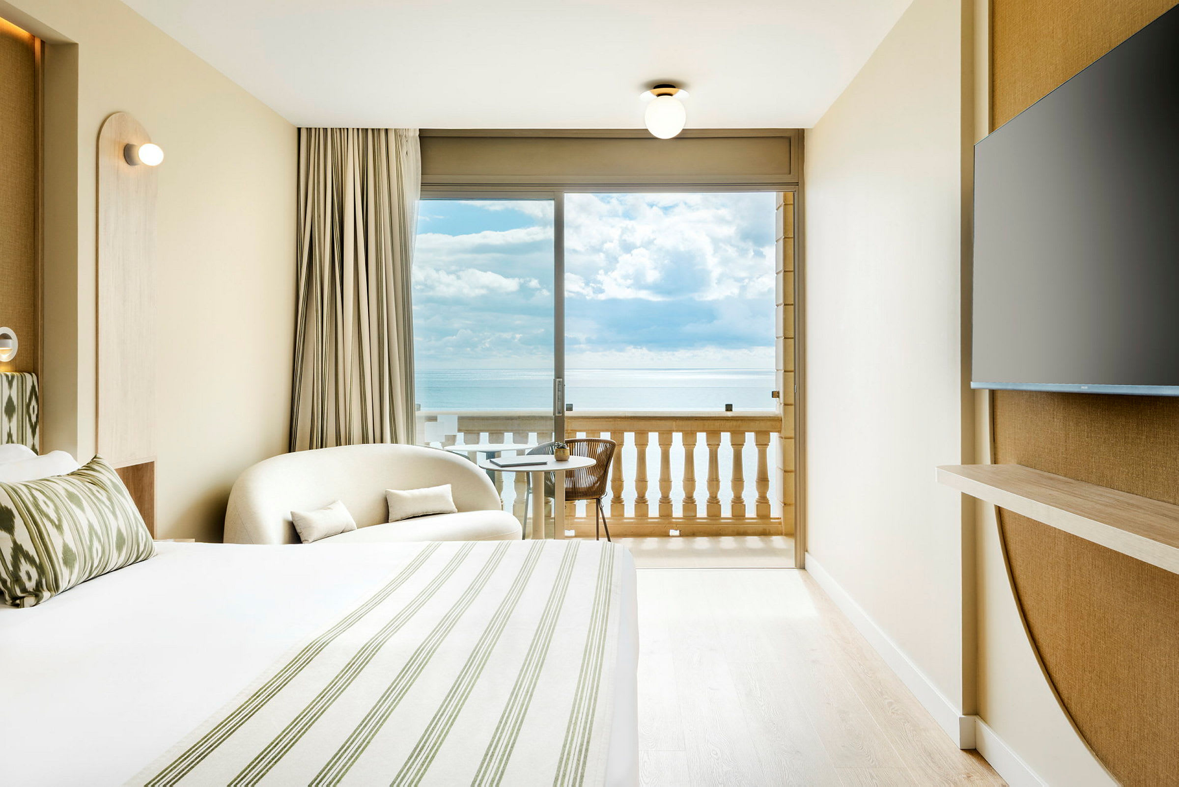 Et hotelværelse med havudsigt fra balkonen. Et stort vindue vender ud mod havet. (AI-genereret tekst)