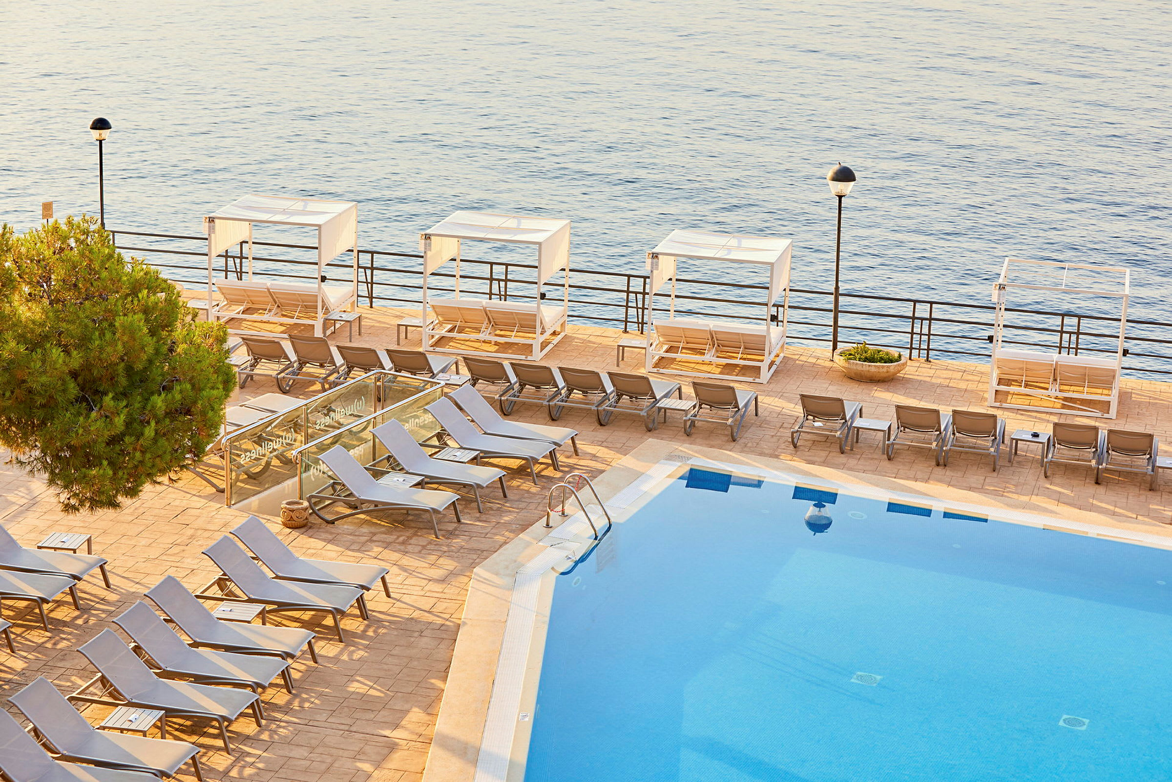 Udendørs pool med solsenge og cabana ved havet. (AI-genereret tekst)