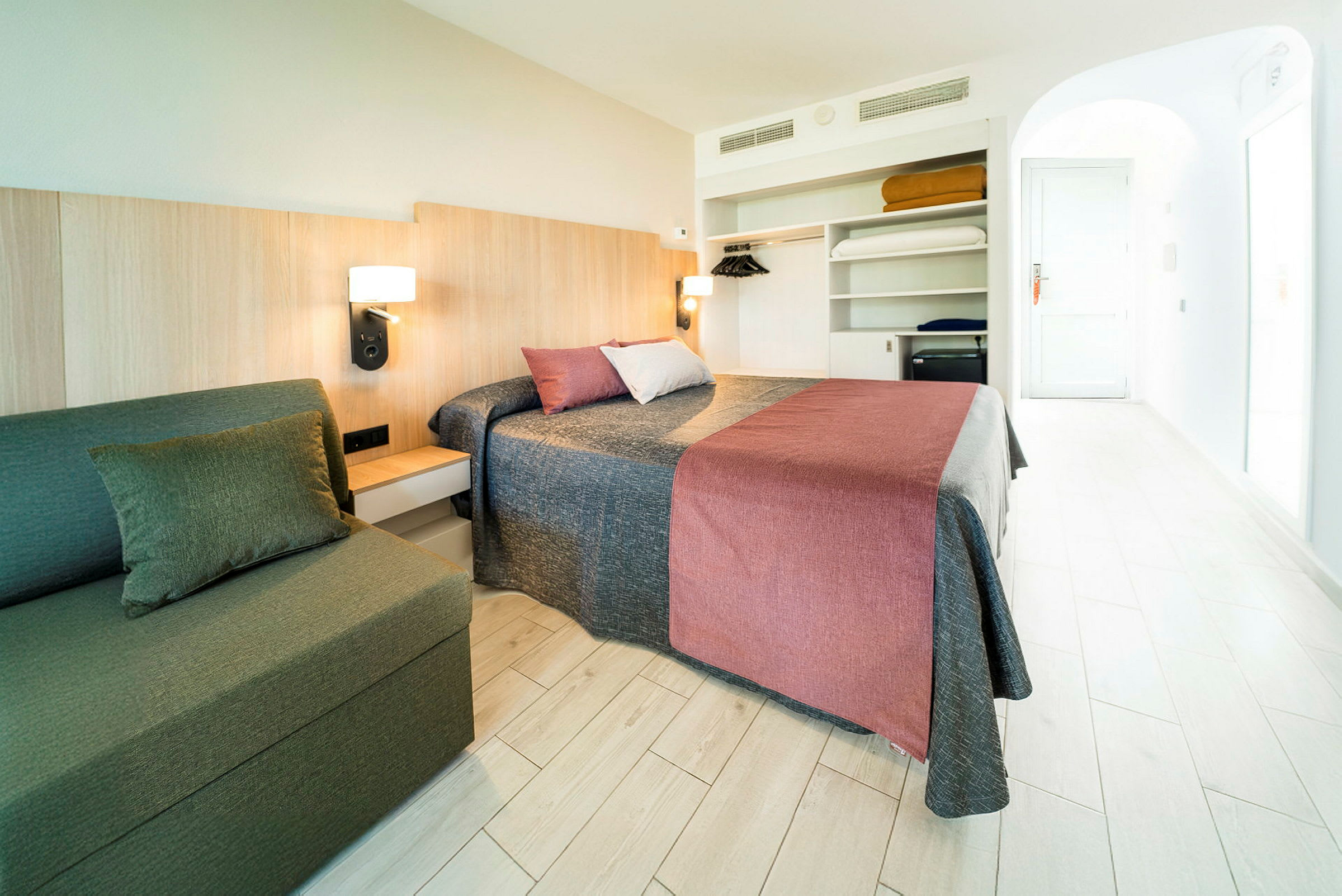 Et hotelværelse med en dobbeltseng, en sofa og en åben garderobe. (AI-genereret tekst)