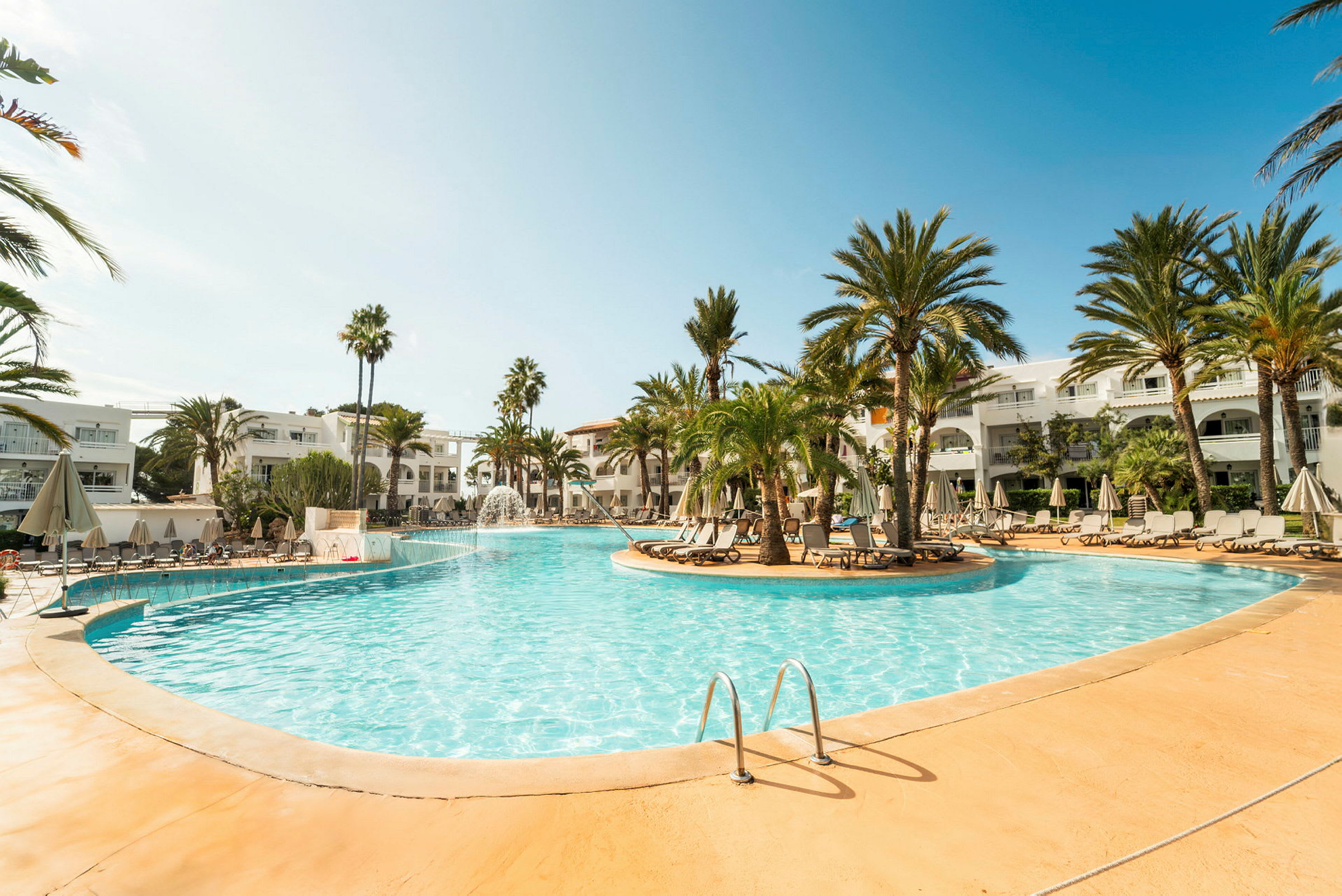 En swimmingpool omgivet af palmer og liggestole på et hotelområde. (AI-genereret tekst)