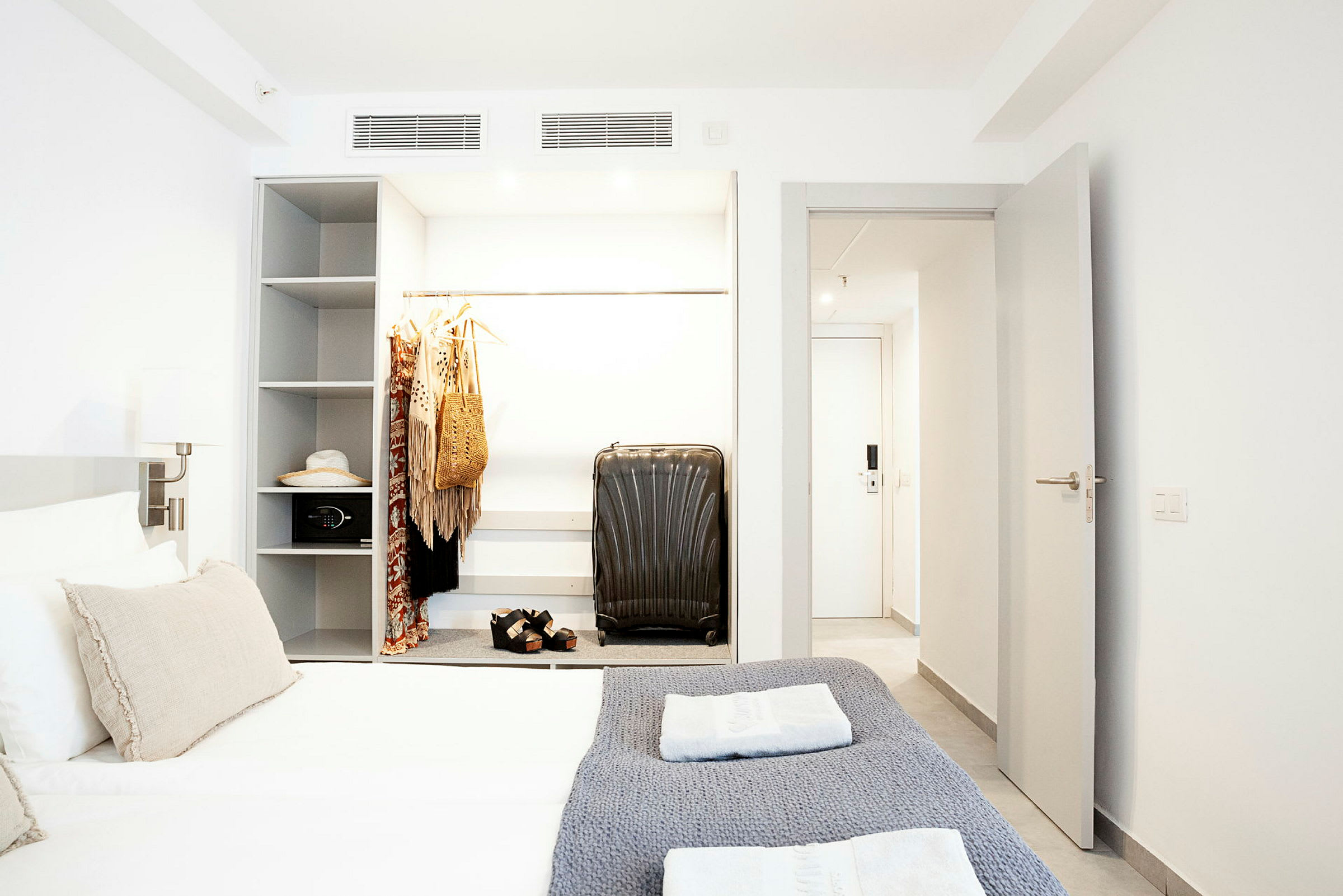 Et hotelværelse med en seng, garderobe med hængende tøj og en kuffert. (AI-genereret tekst)