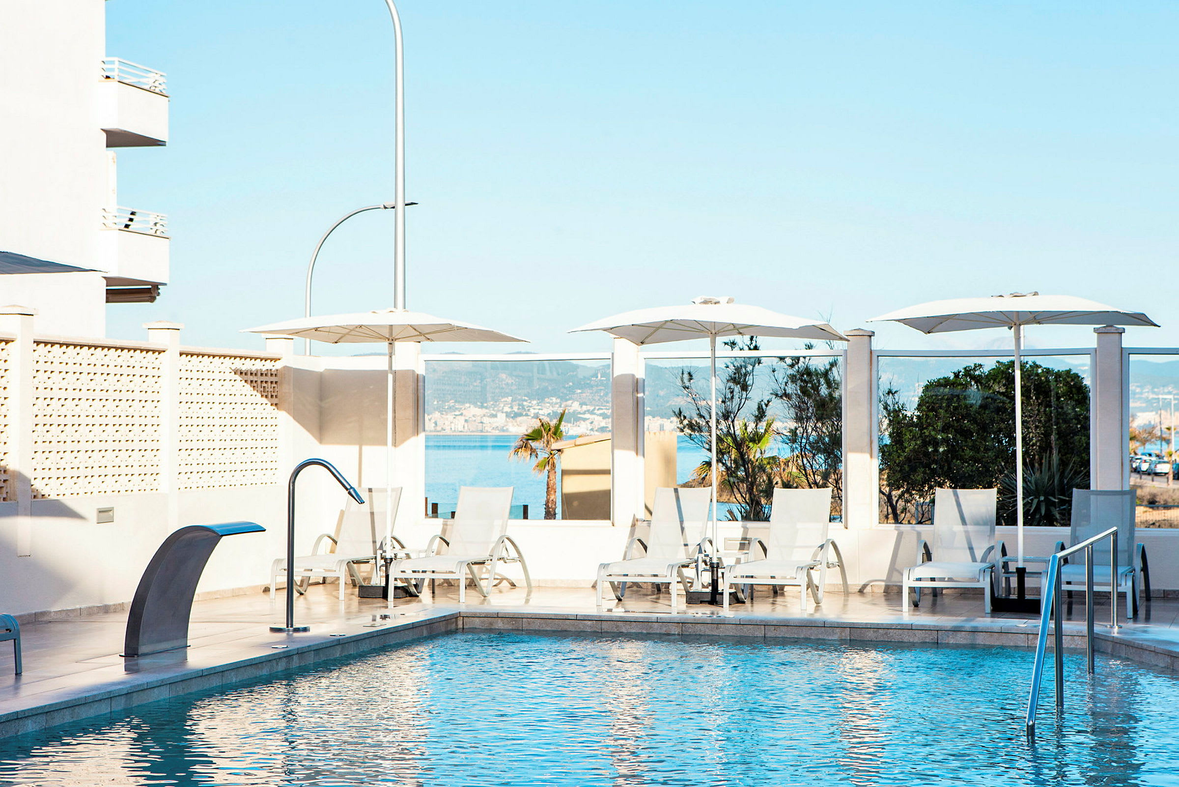 Udendørs pool med liggestole og parasoller, omgivet af en terrasse og havudsigt. (AI-genereret tekst)