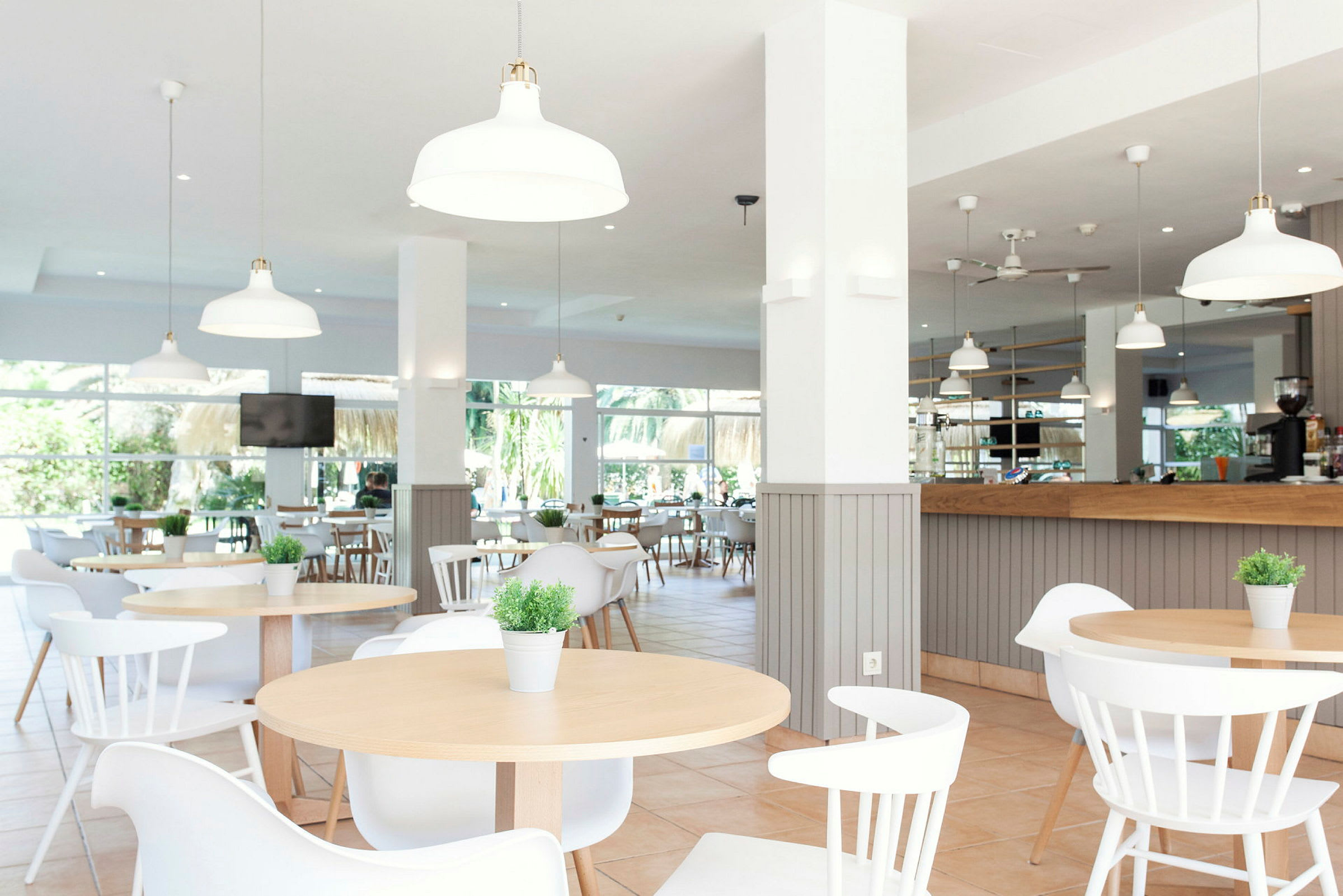 Billede af en moderne, lys restaurant med borde, stole og dekorative planter. (AI-genereret tekst)