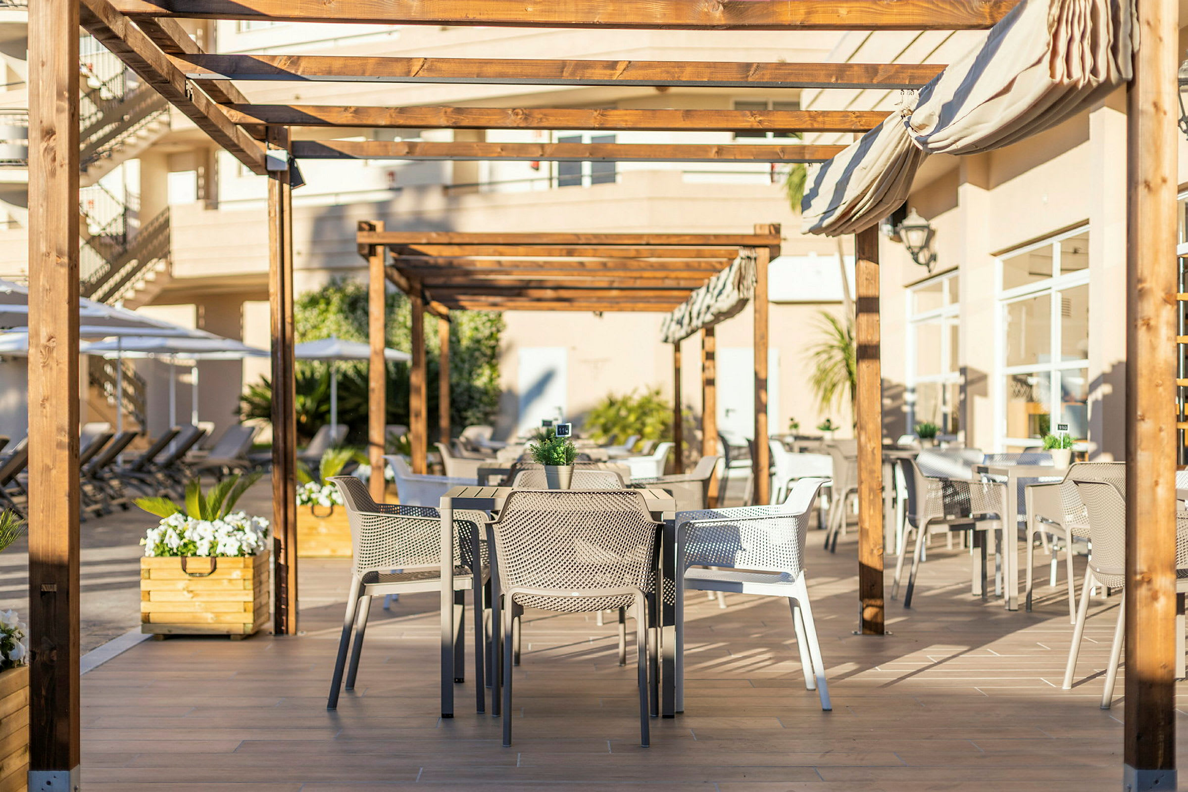 Udendørs serveringsområde under træpergola med borde og stole. (AI-genereret tekst)
