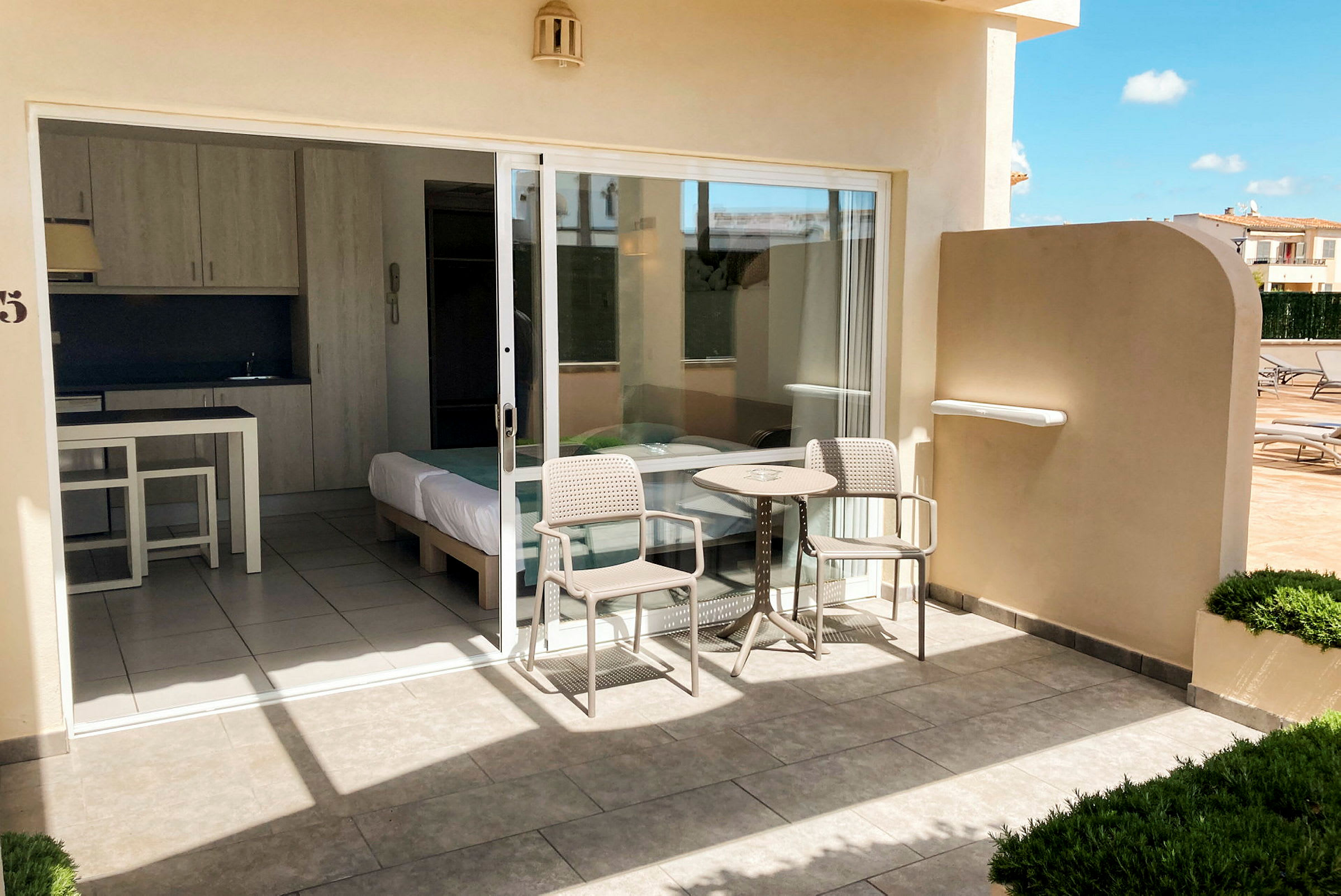 Terrasse med bord og stole foran et hotelværelse med glasdør. (AI-genereret tekst)